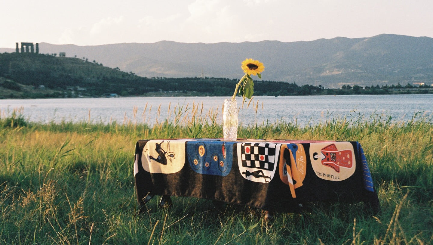 Decorative tablecloth with various patterns, japanese aesthetic on a grassy field with a lake and mountains in the background.