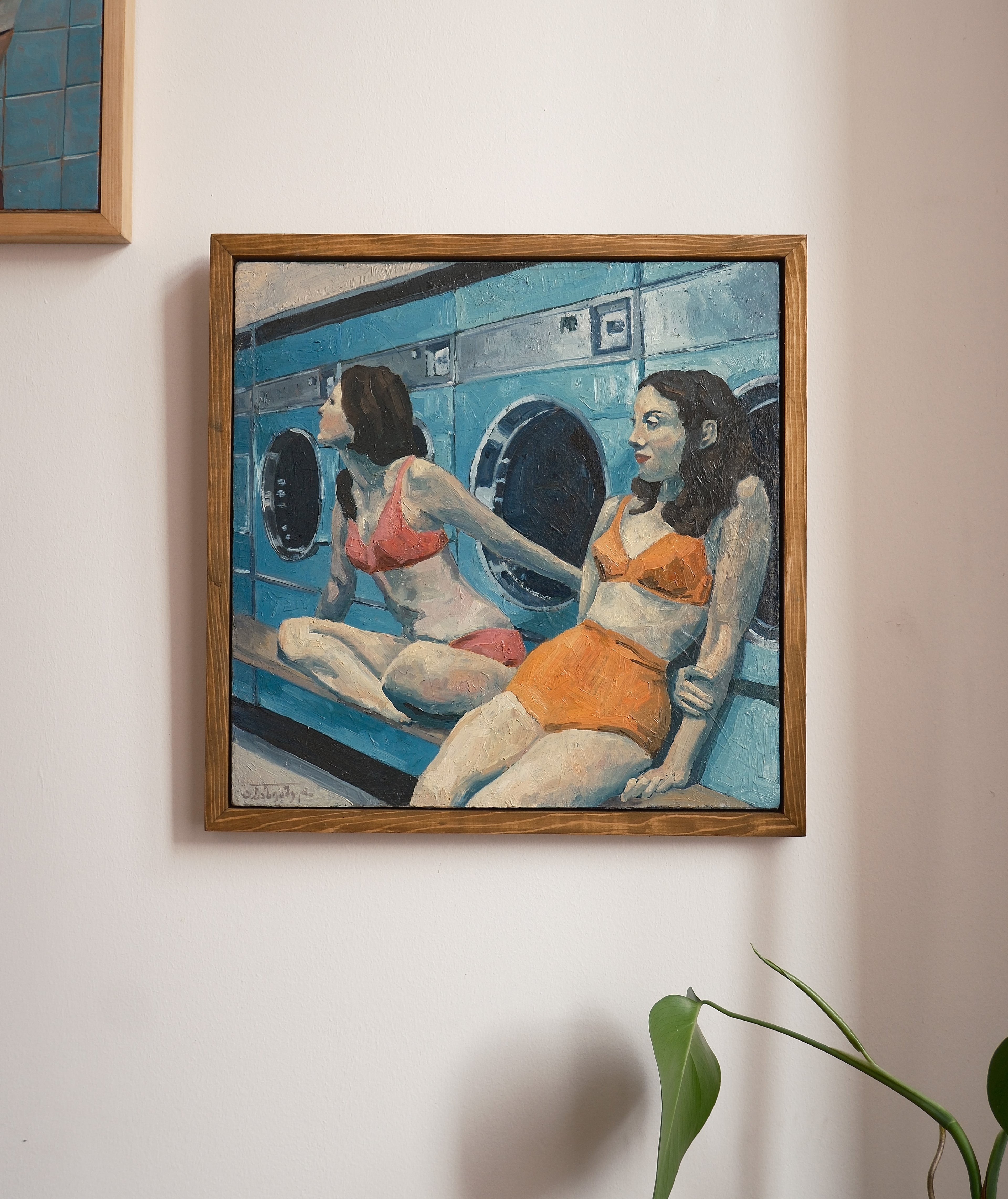 Framed artwork of two women in a laundromat on a wall.