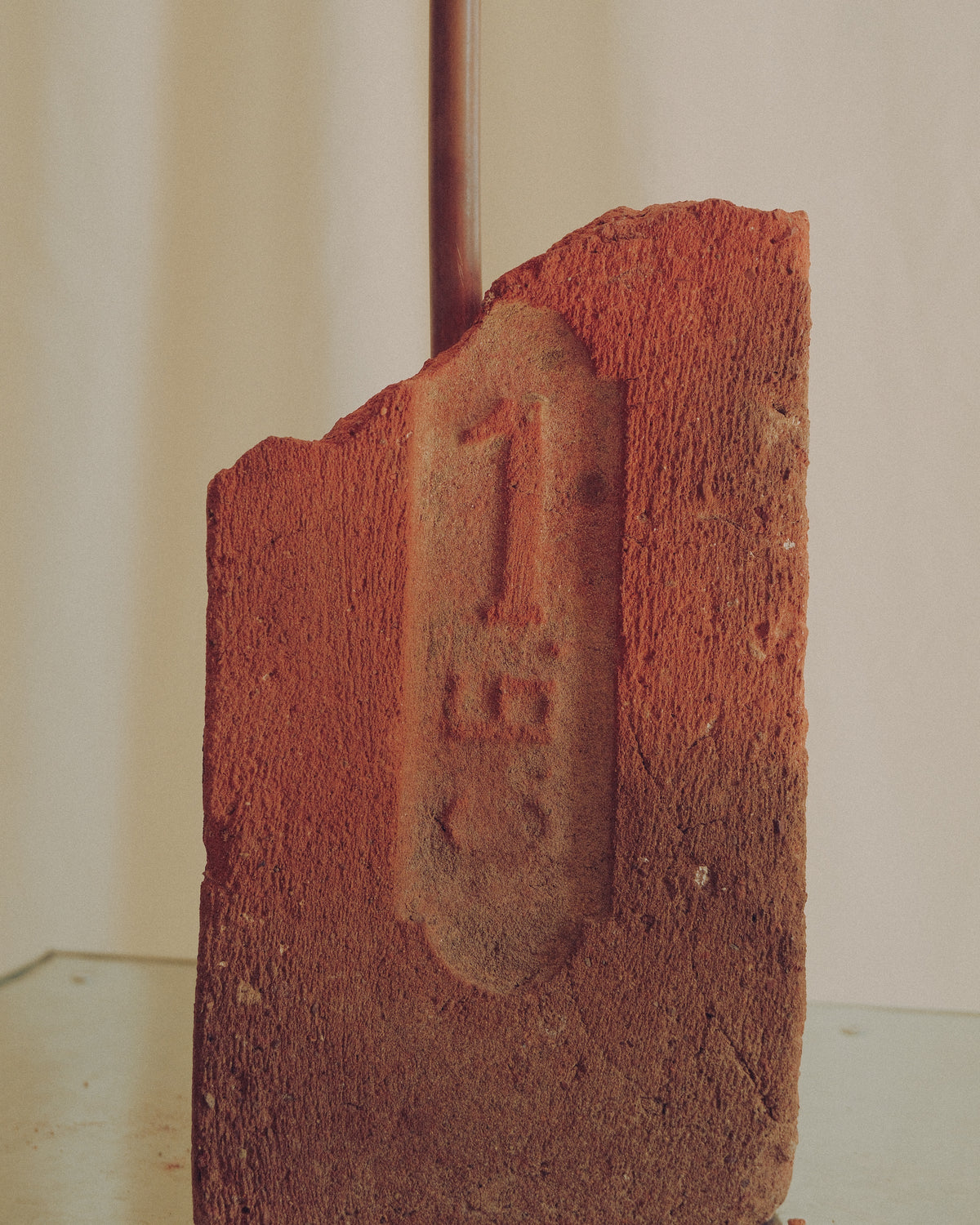 A close-up of a textured terracotta clay or brick-like object with a carved or embossed number '1' on the front, standing upright against a plain light background.
