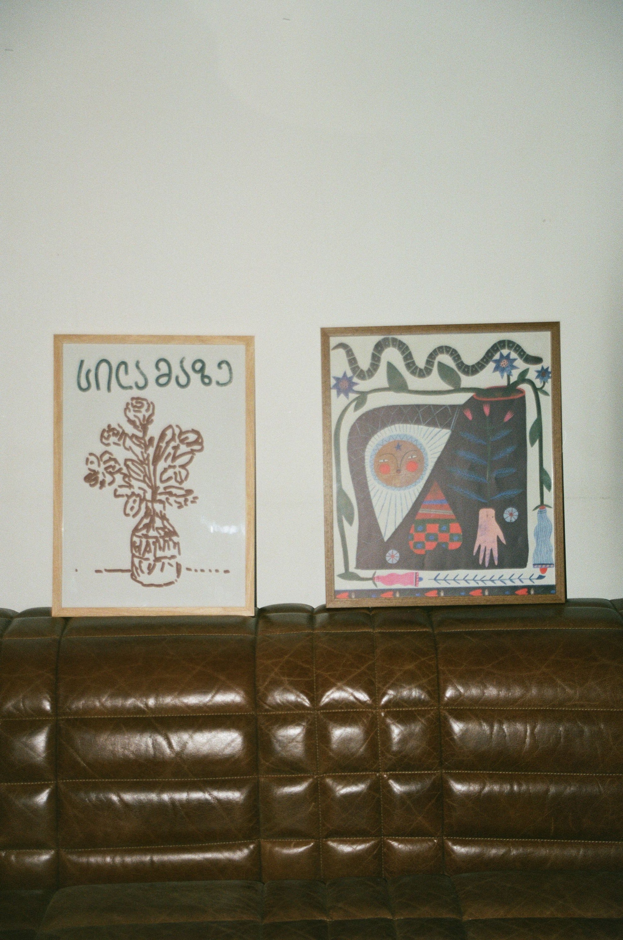 Two framed artworks on a wall next to a brown textured surface.