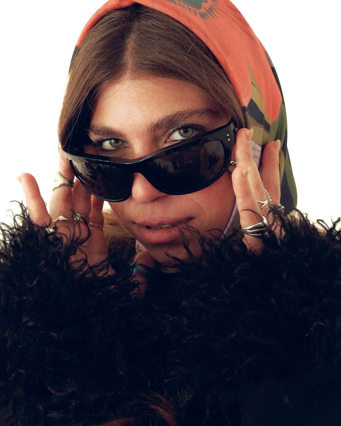 Person wearing sunglasses and a colorful headscarf with a dark fur collar.