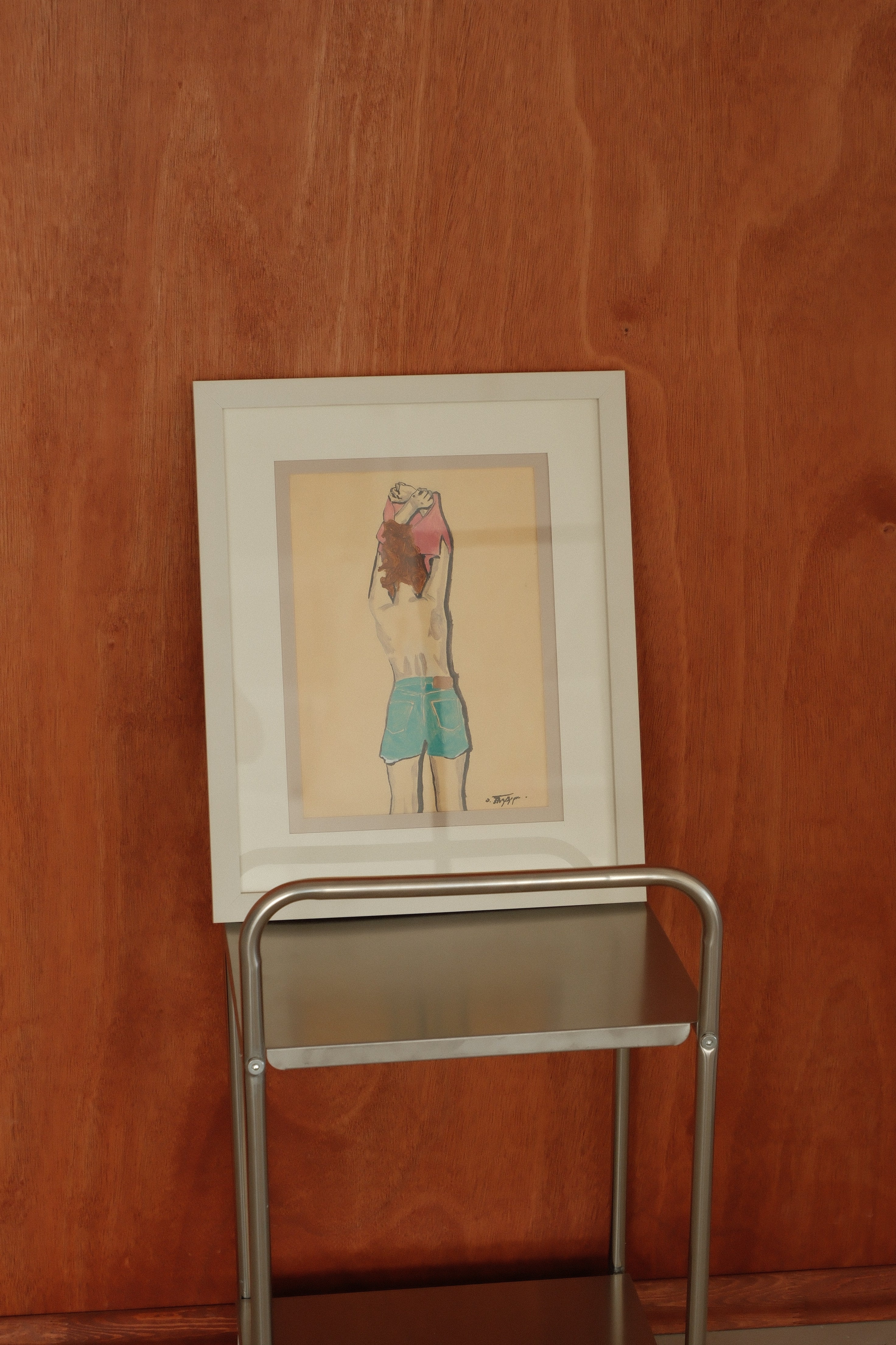 Framed artwork of a person in green shorts on a metal stand against an orange wall.