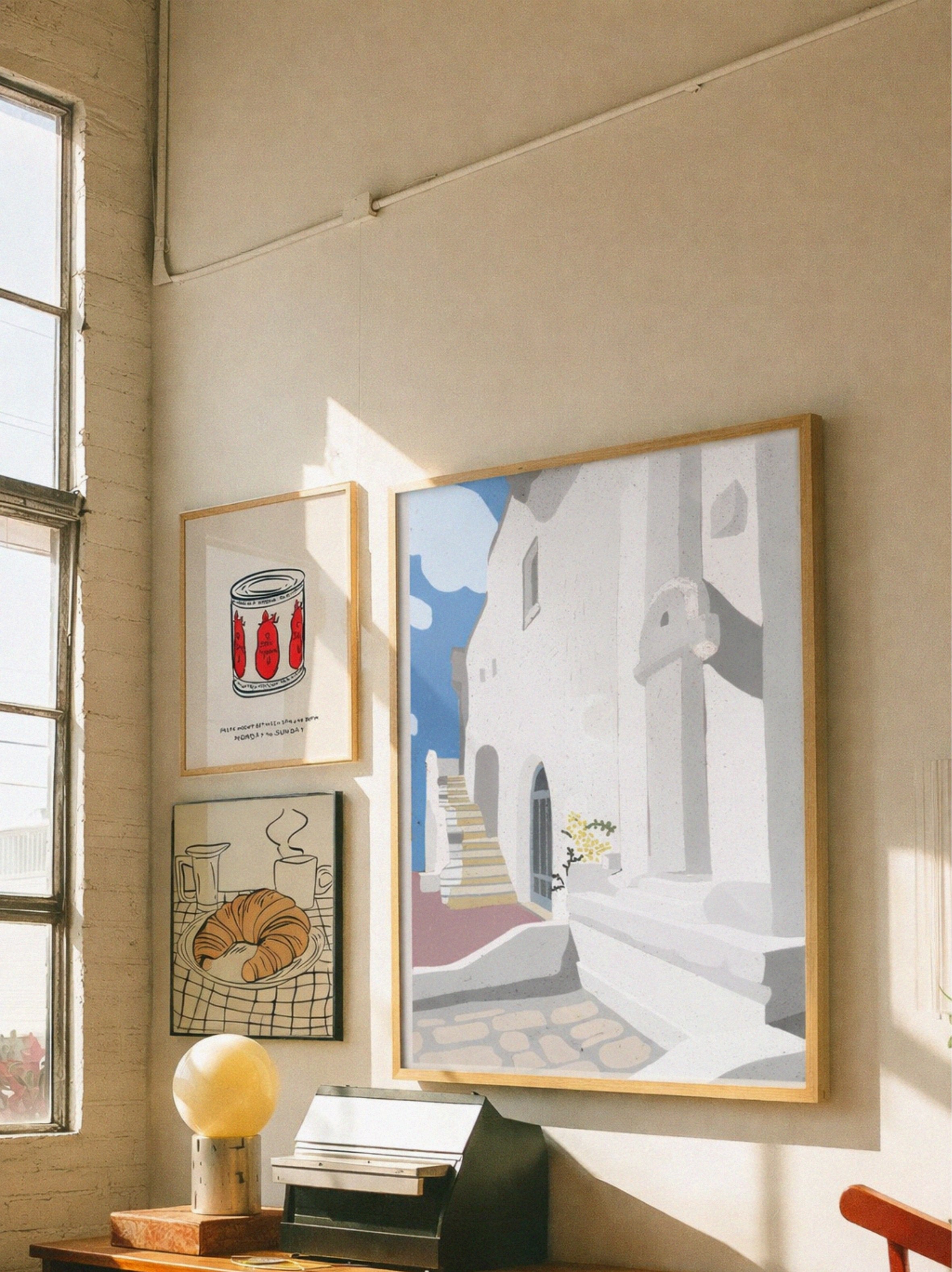 Three framed artworks on a wall with natural light coming through a window.