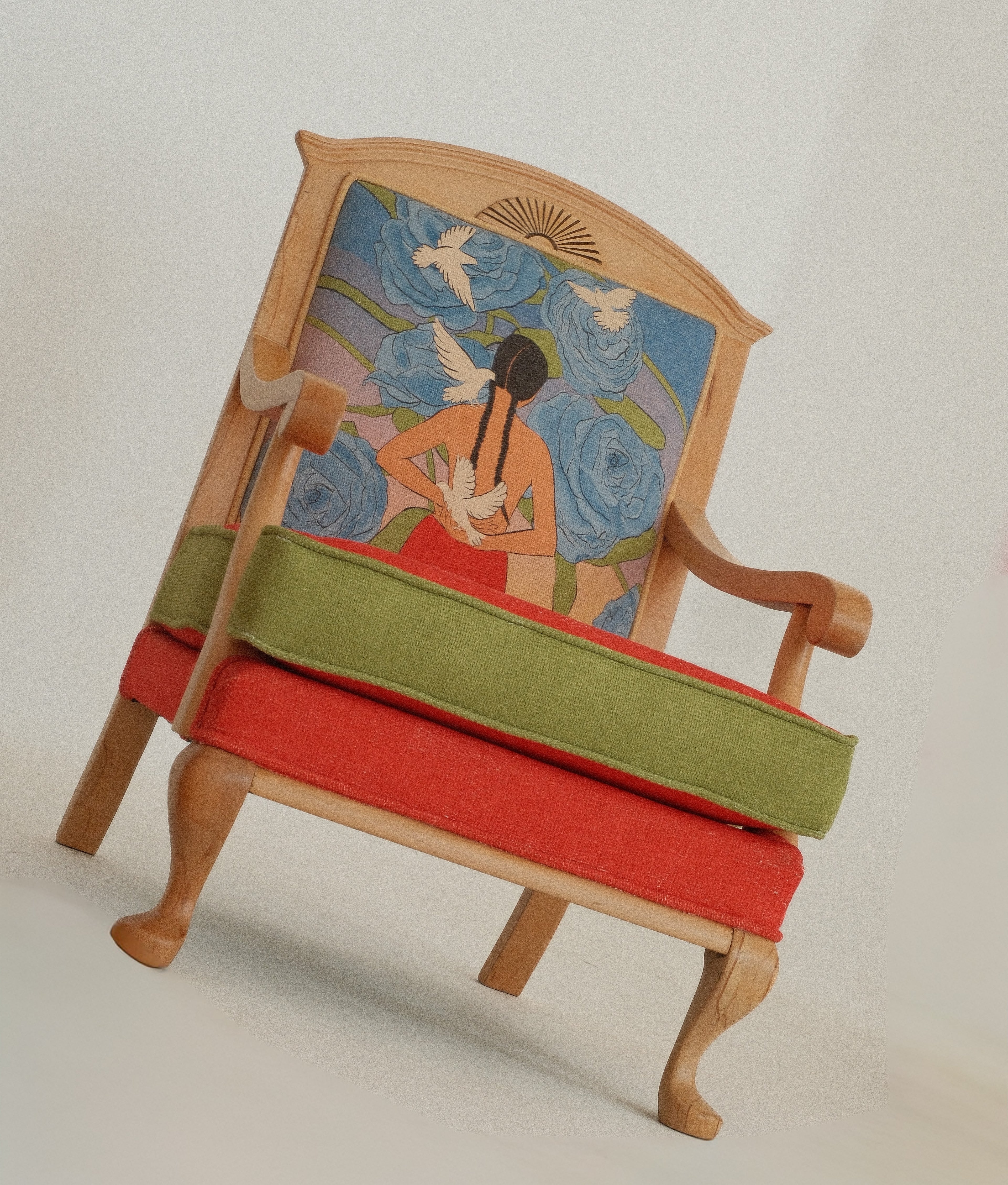 A vintage-style wooden armchair with a light natural wood frame, featuring a red upholstered seat cushion, a green upholstered back cushion, and a highly detailed, colorful painted backrest depicting a woman with doves.