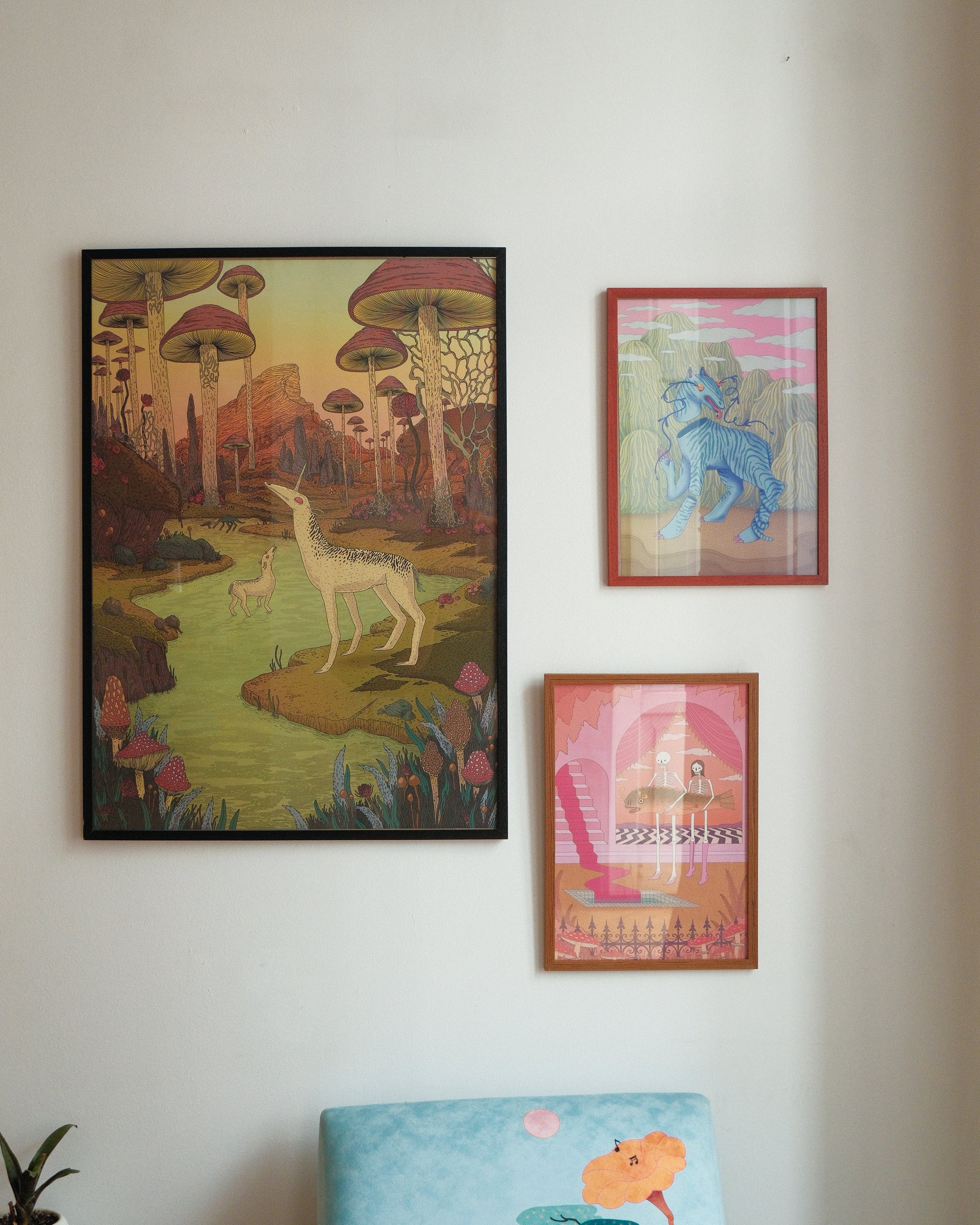 Three colorful framed artworks on a wall with a light blue cushion in the foreground.