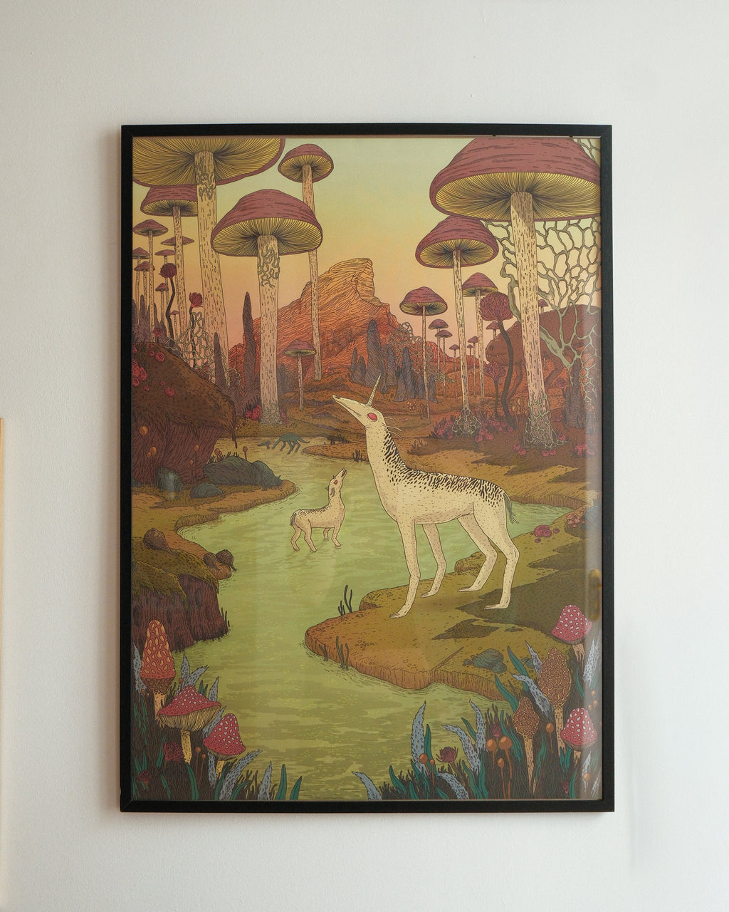 Framed artwork of a deer in a fantasy forest with mushrooms on a white wall.