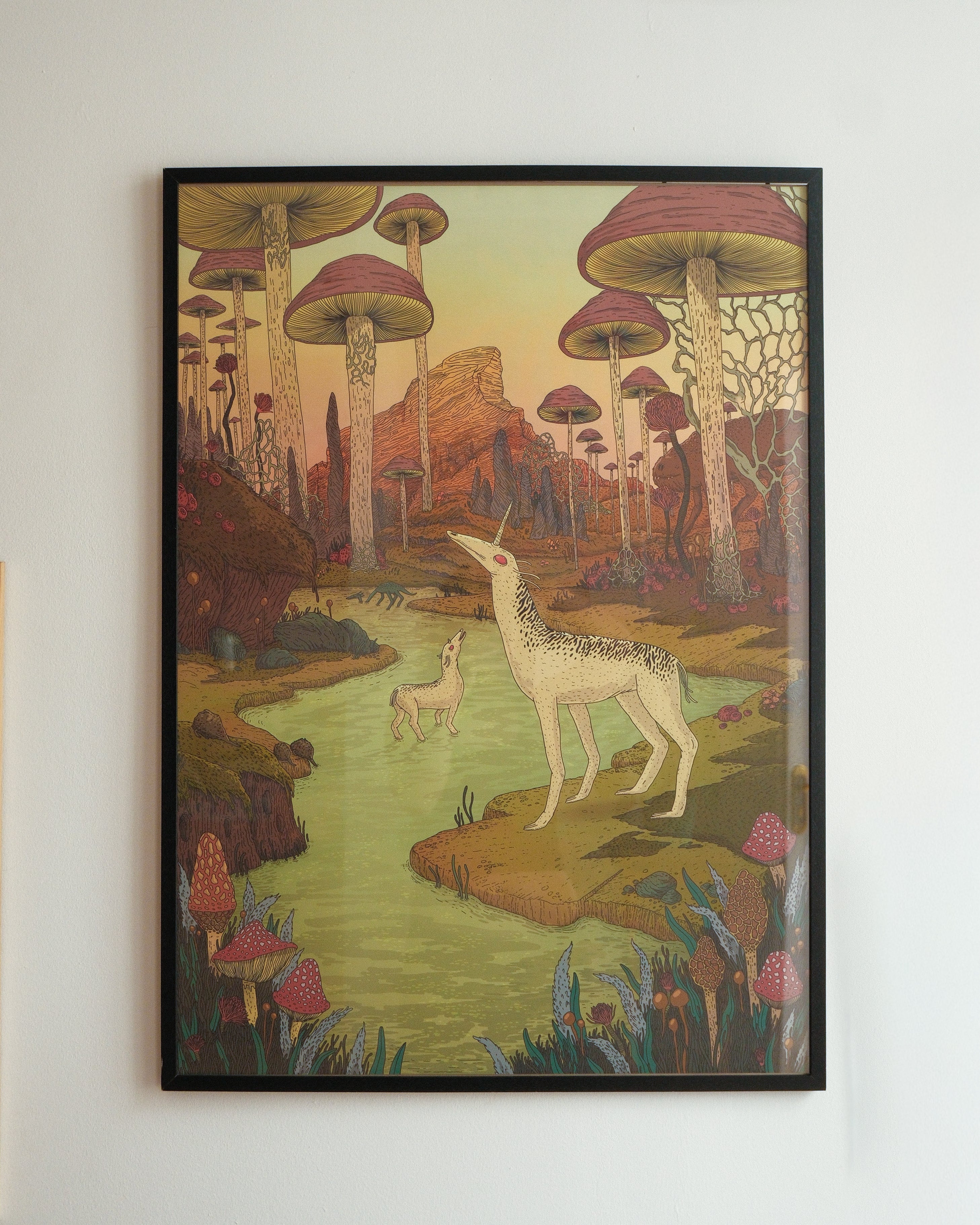 Framed artwork of a deer in a fantasy forest with mushrooms on a white wall.