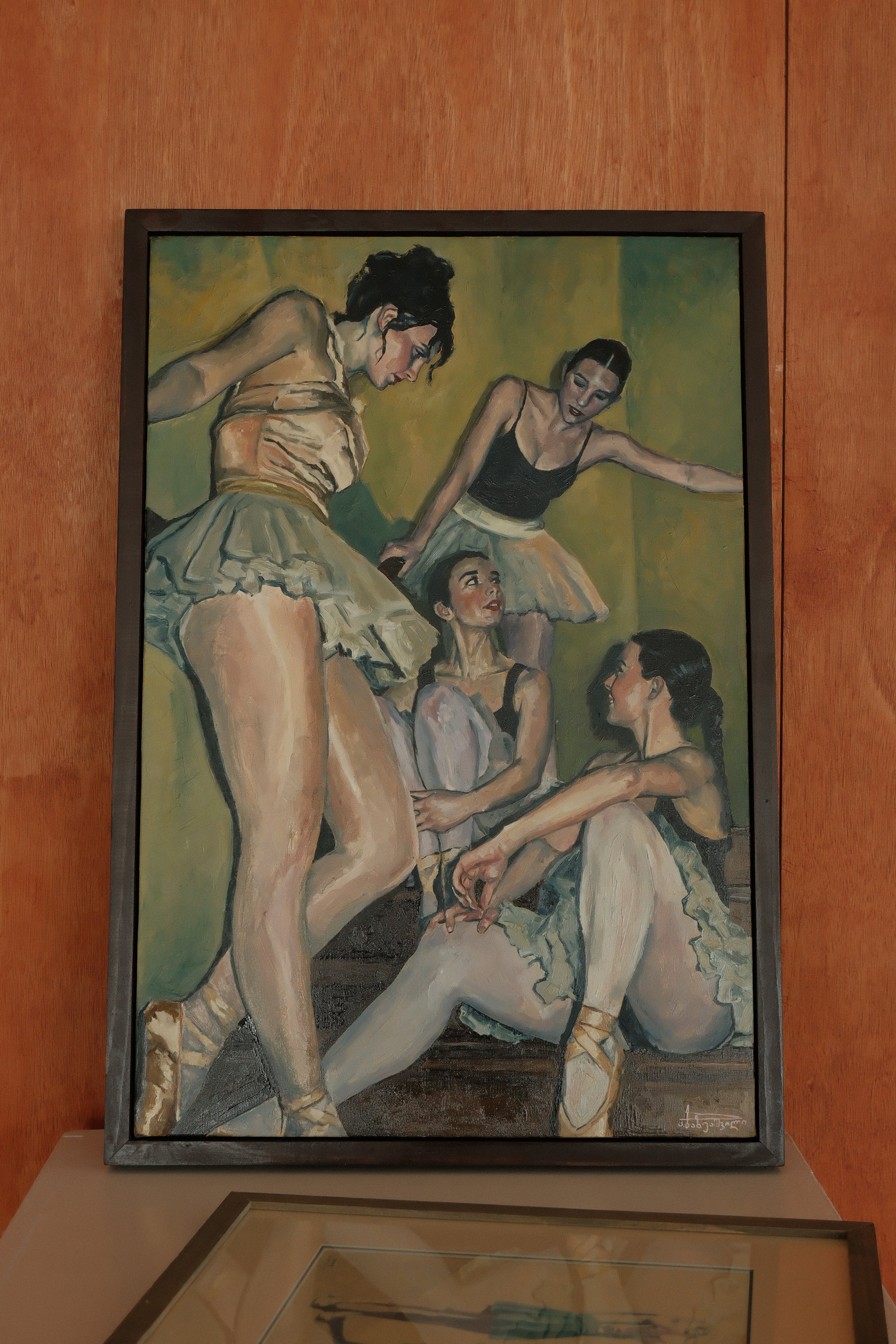 Framed artwork of ballerinas on a wooden surface, another painting is seen there too