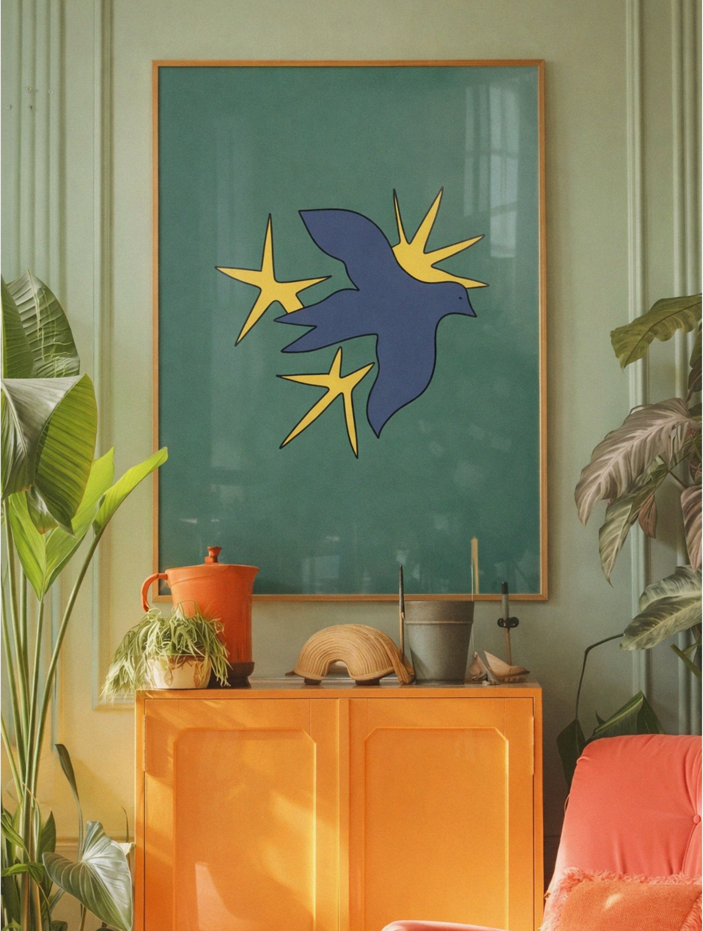Abstract artwork of a blue bird with yellow stars on a green background, displayed in a room with plants and furniture.