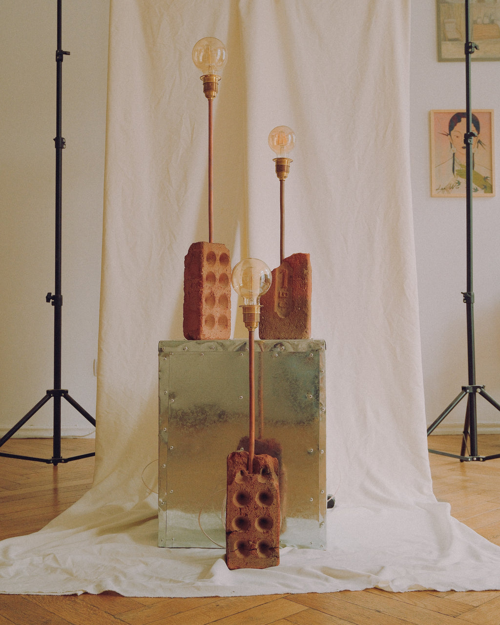 Three rustic industrial table lamps with exposed Edison bulbs, featuring brick-shaped shades and a vintage metal trunk base, set against a draped white fabric backdrop.
