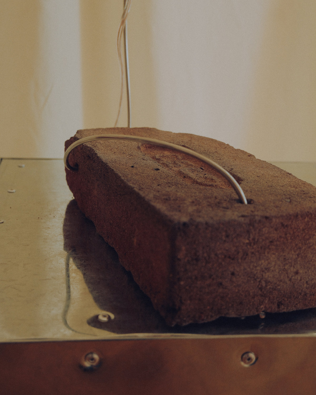 A rustic rectangular brick or stone block with a curved metal loop attached, resting on a metallic surface against a plain light background.