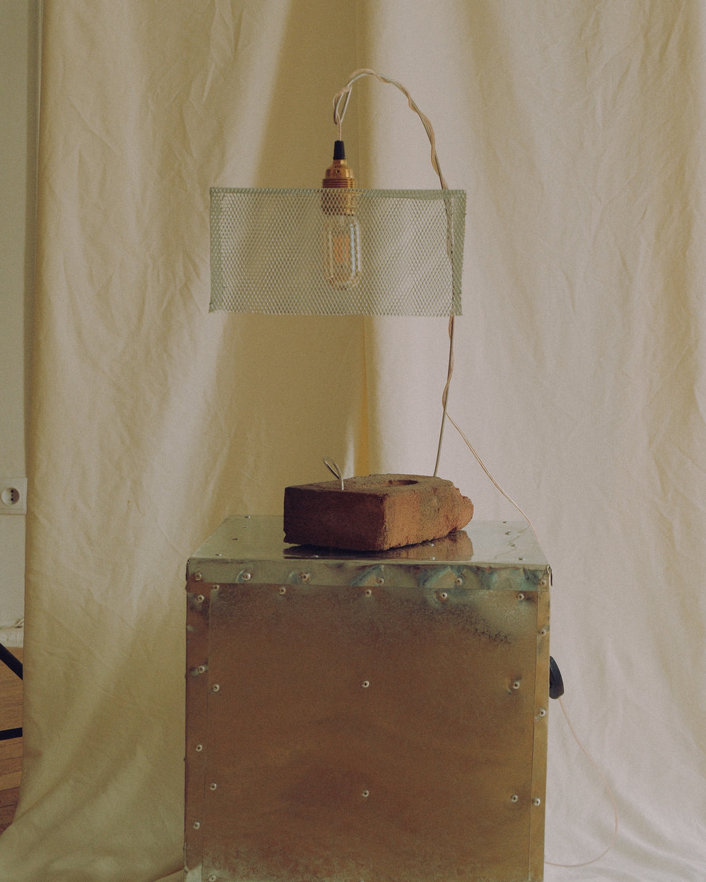 Handmade “Tether” lamp with a reclaimed brick base, curved metal structure and suspended mesh shade.
