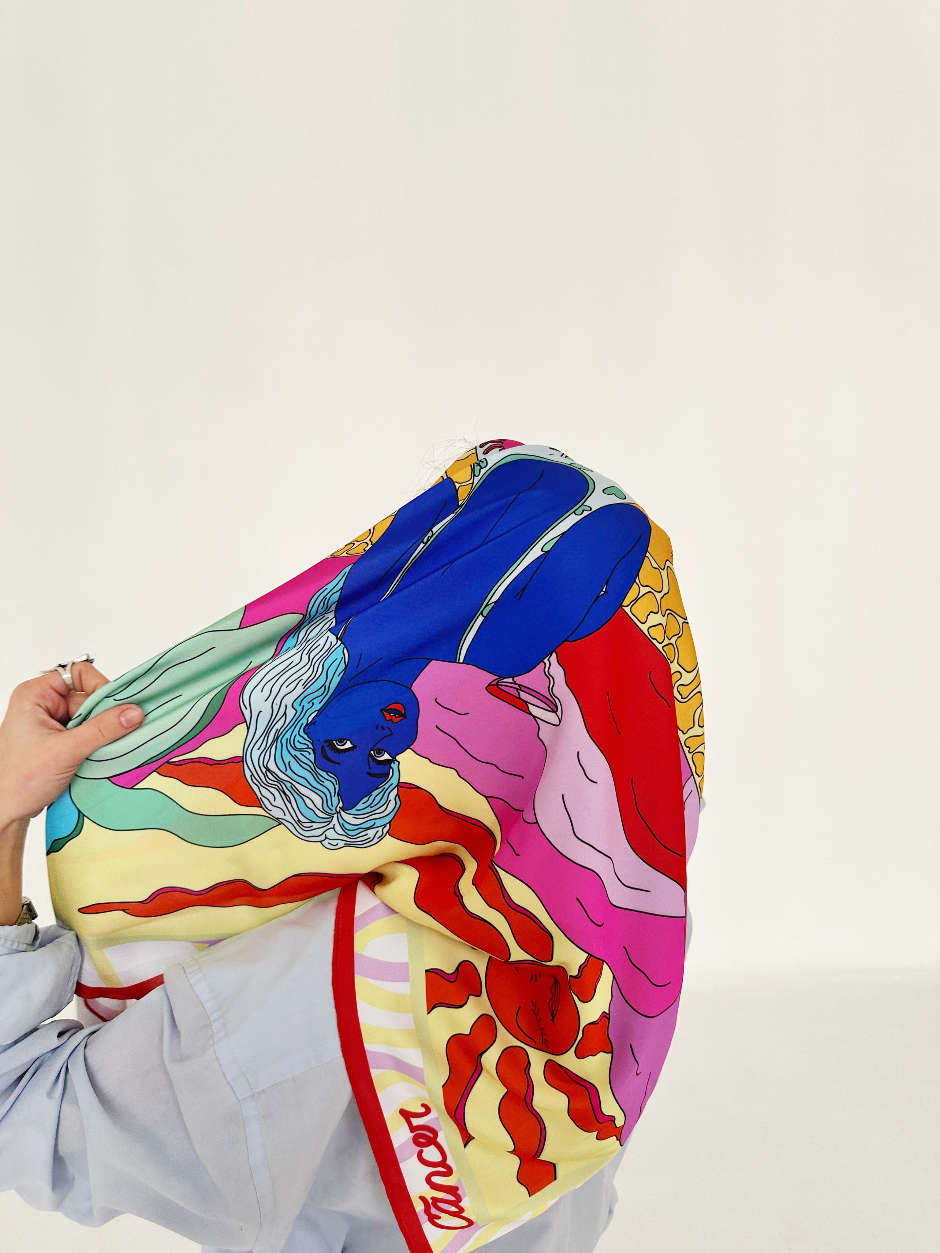 A colorful scarf with abstract and geometric patterns, held up by a person against a white background. Cancer zodiac art silk scarf by Anano Kevanishvili with warm expressive colors