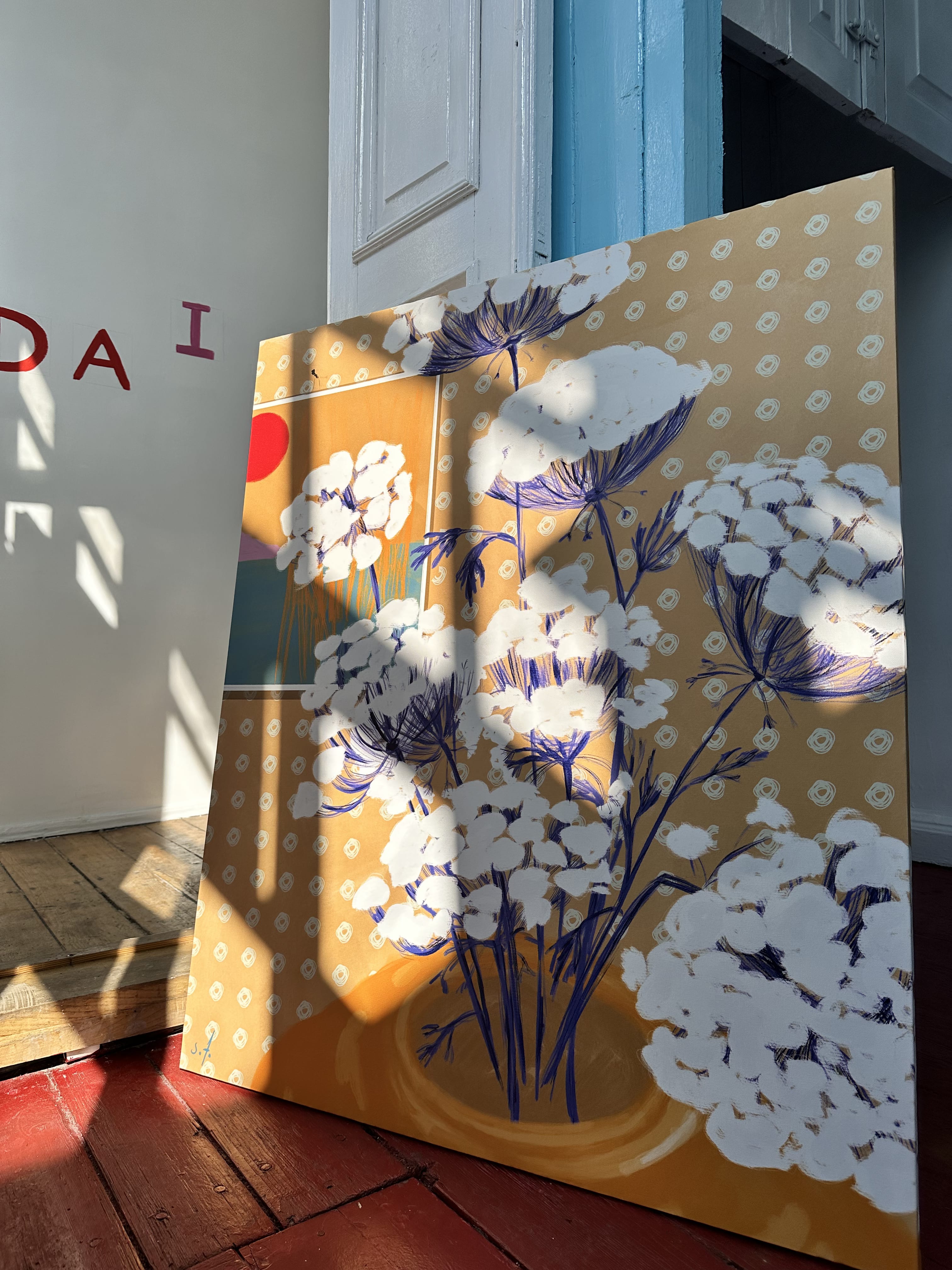 A painting featuring a floral motif with white and blue flowers on a yellow background, placed on a floor with a shadow cast over it.