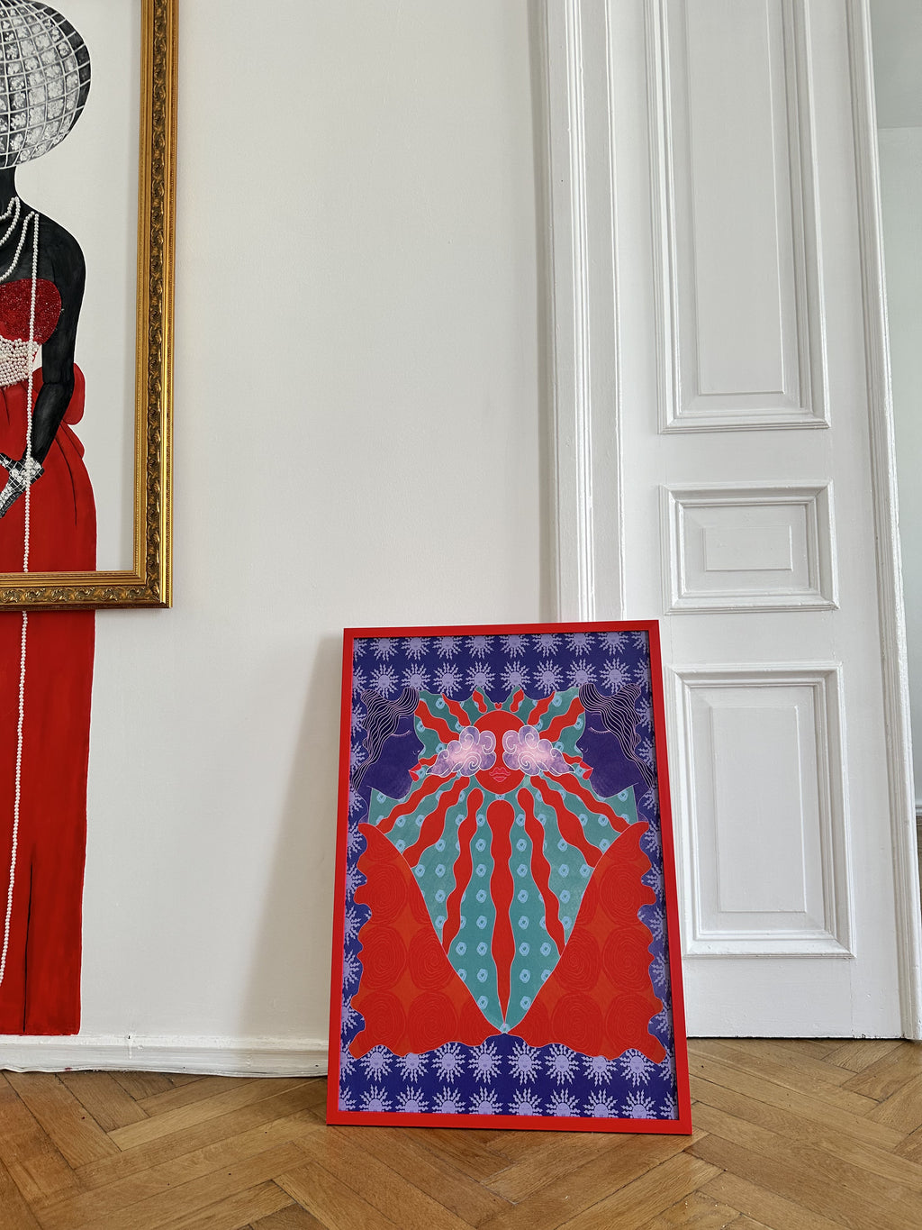 A canvas poster featuring a geometric and floral pattern in red, blue, and purple colors, standing against a wall with an open door leading to a hallway.