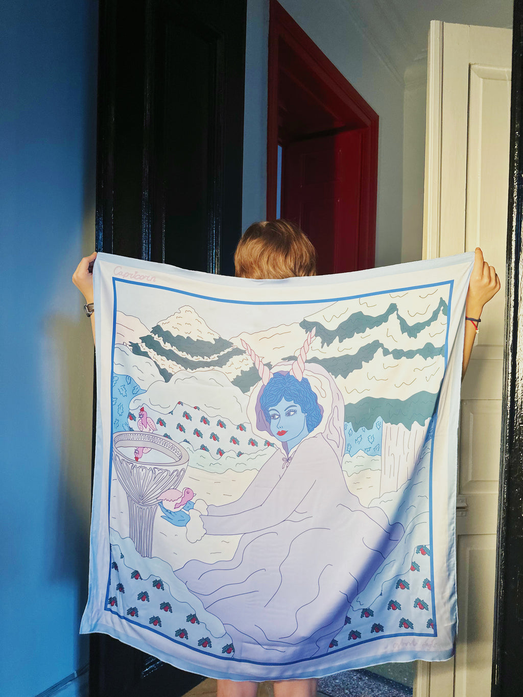 Capricorn zodiac art silk scarf hanging flat, showing detailed pastel blue and neutral-toned artwork