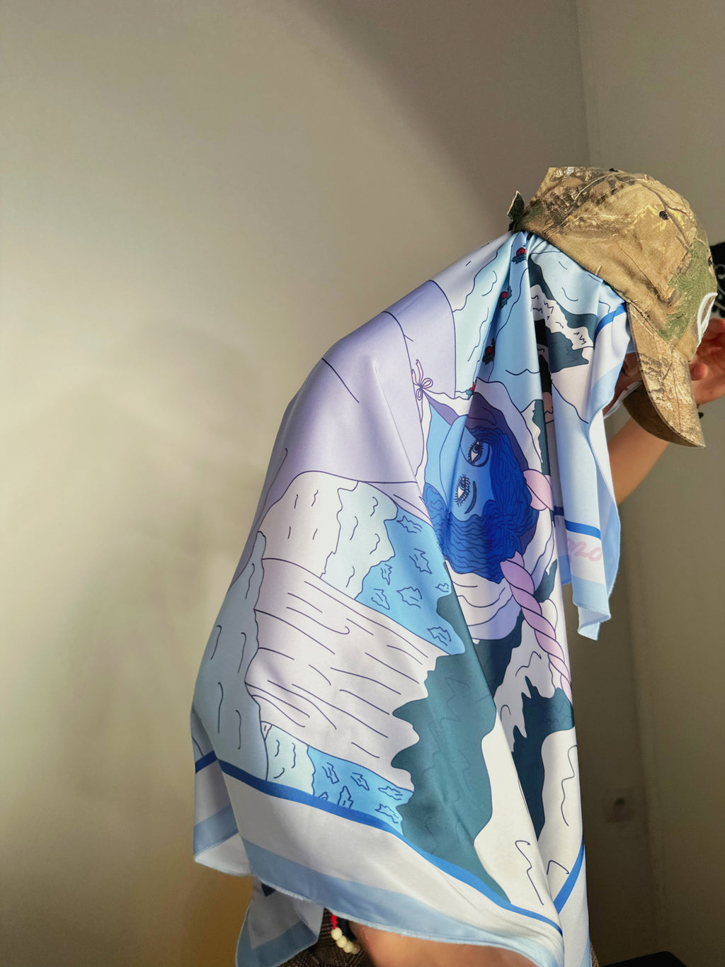 Capricorn zodiac scarf styled on model with elegant blue illustration and gentle patterns, model wearing it with hat
