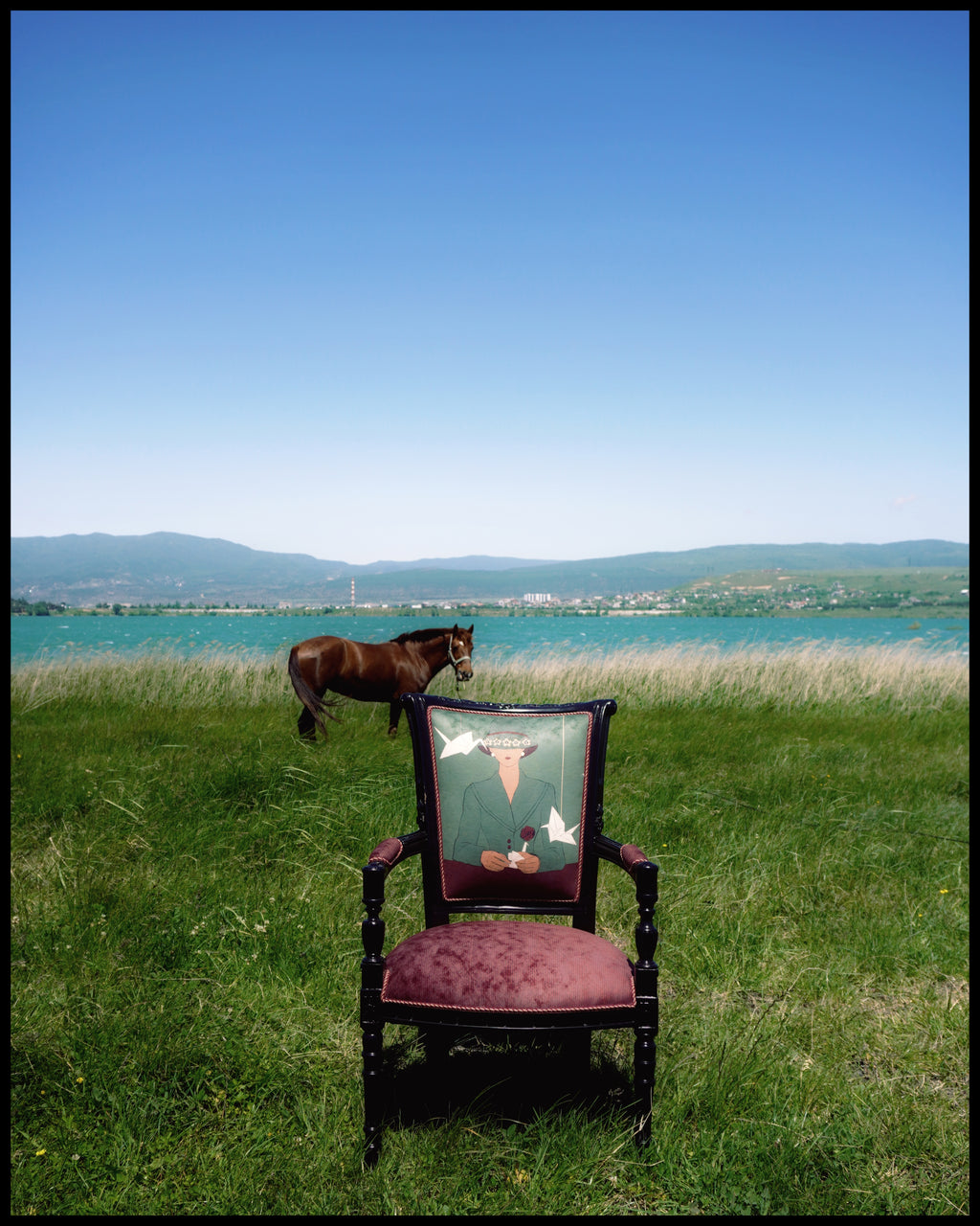 Chair with a decorative backrest in a grassy field with a horse in the background.