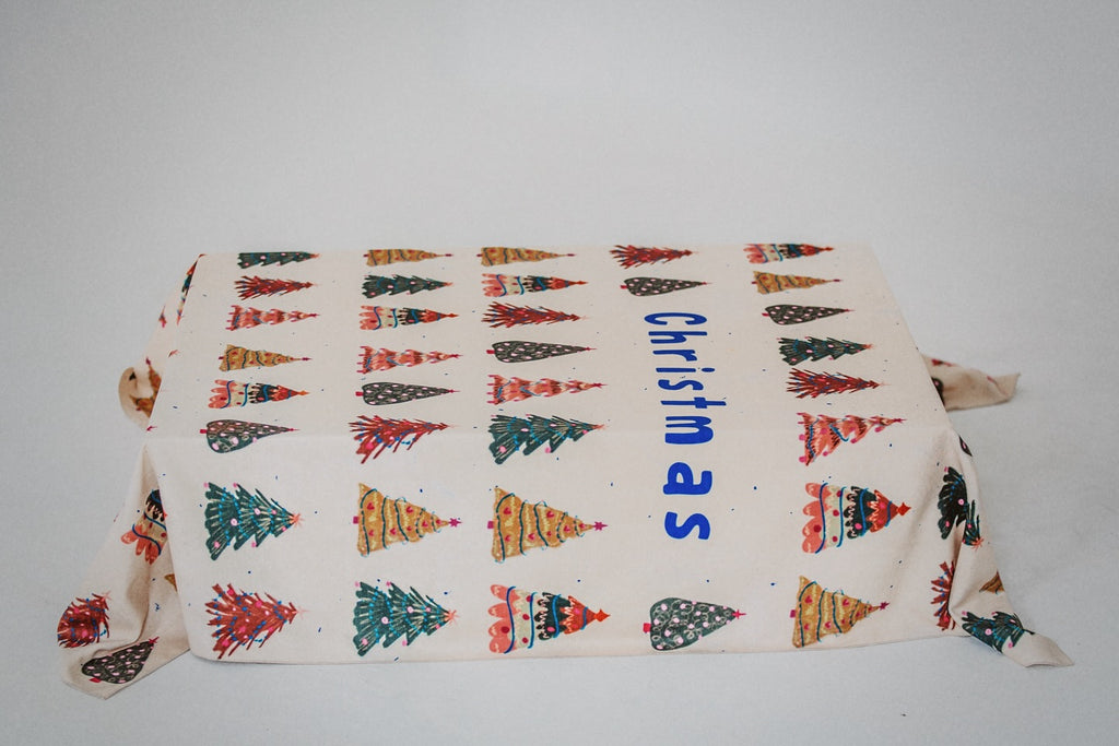 A Christmas-themed tablecloth featuring a repeated pattern of illustrated Christmas trees with decorative elements, and the word 'Christmas' written across the bottom.