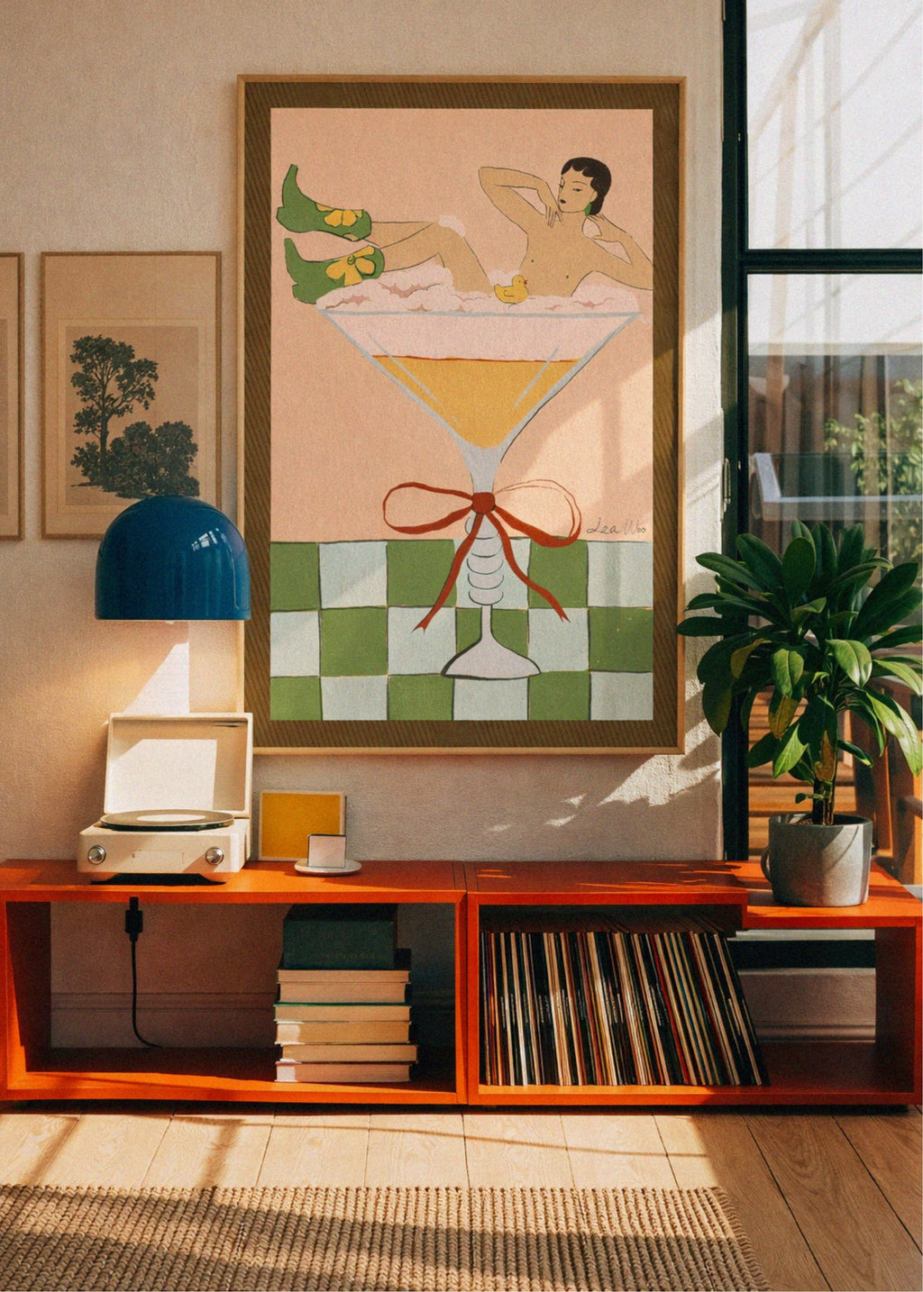 Room interior with a large framed artwork of a woman in a martini glass, orange shelf with records and books, and a plant.