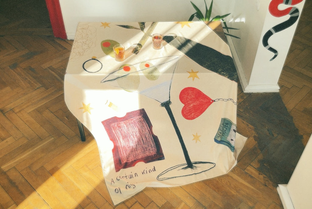 A tablecloth featuring various illustrations including a cocktail glass and abstract designs, laid out on a table.