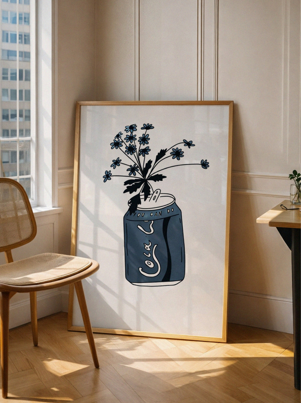 Framed artwork of a blue mason jar with flowers on a wall in a room with a chair and window.