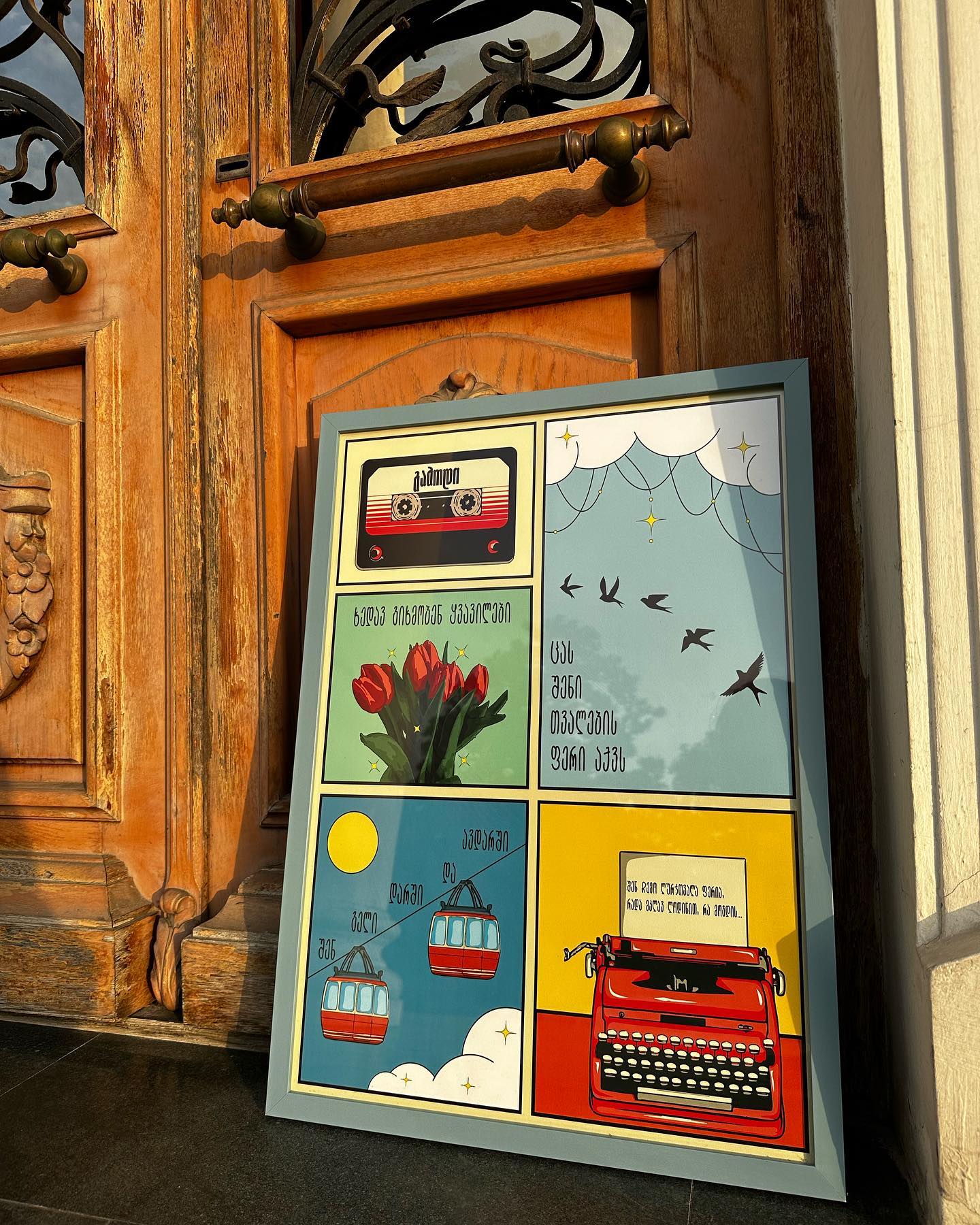 A colorful poster with various cultural symbols and a vintage typewriter, displayed on a wooden door. Poster “Come Out” by Mariam Kantaria – Georgian song-inspired wall art by DAE • დაე