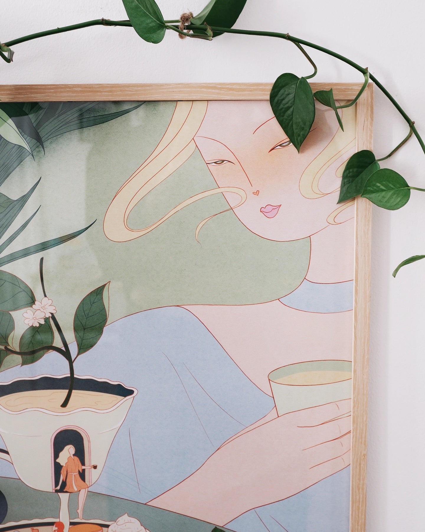 Framed illustration of a woman holding a cup, surrounded by green leaves.