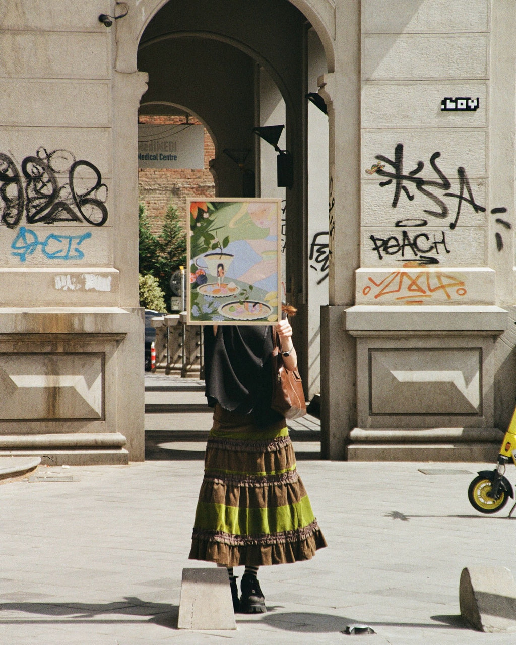 Person holding a painting in an urban setting with graffiti on walls.