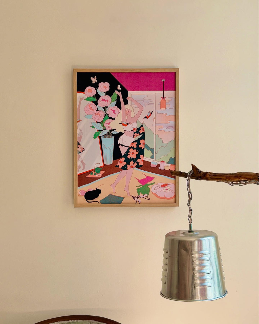 Framed “Dancing at Home” art poster hung on a wall above a silver lamp in a cozy interior space.
