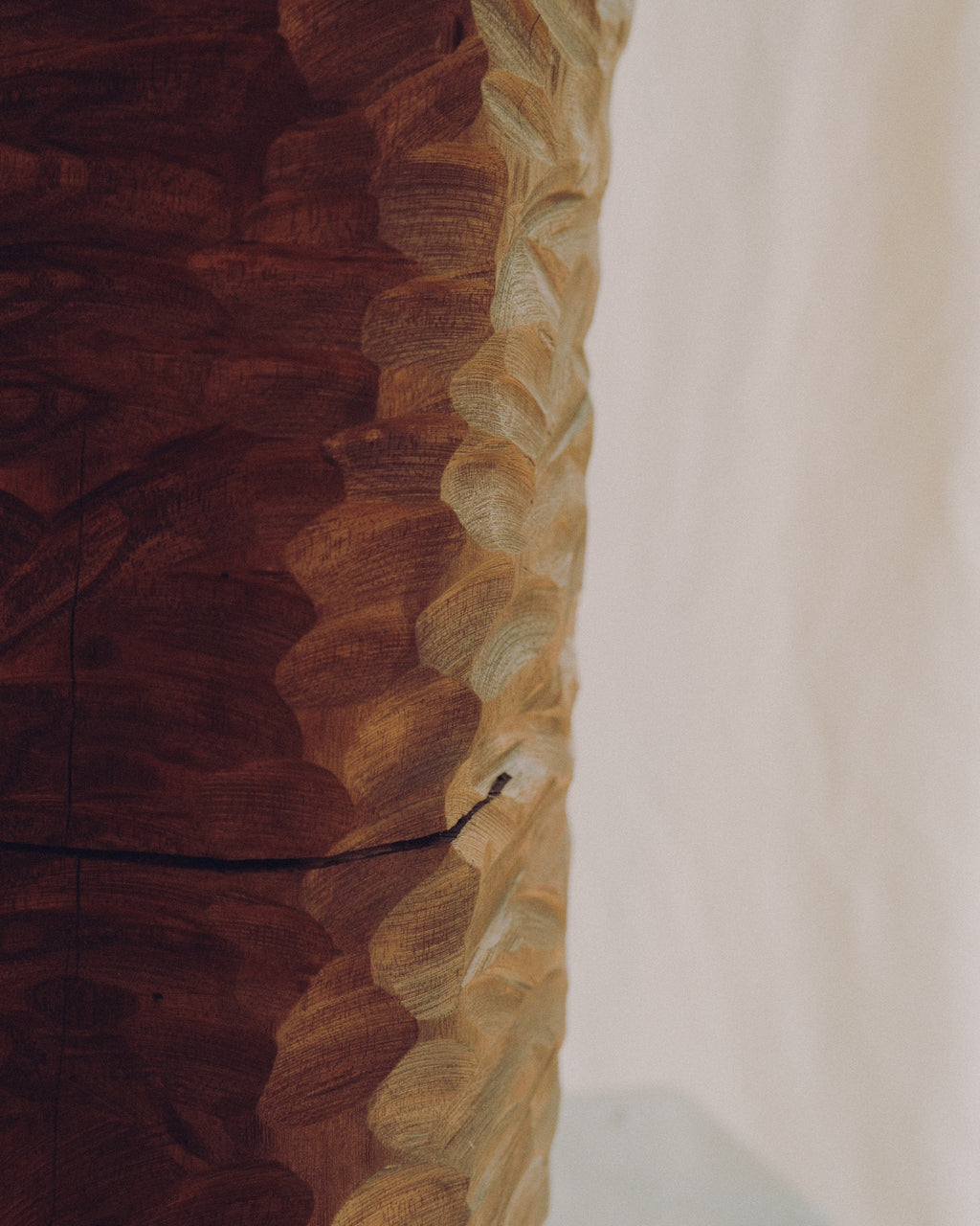 A close-up of a carved wooden object with a richly textured, wavy edge showing contrasting dark and light wood tones against a plain off-white background.