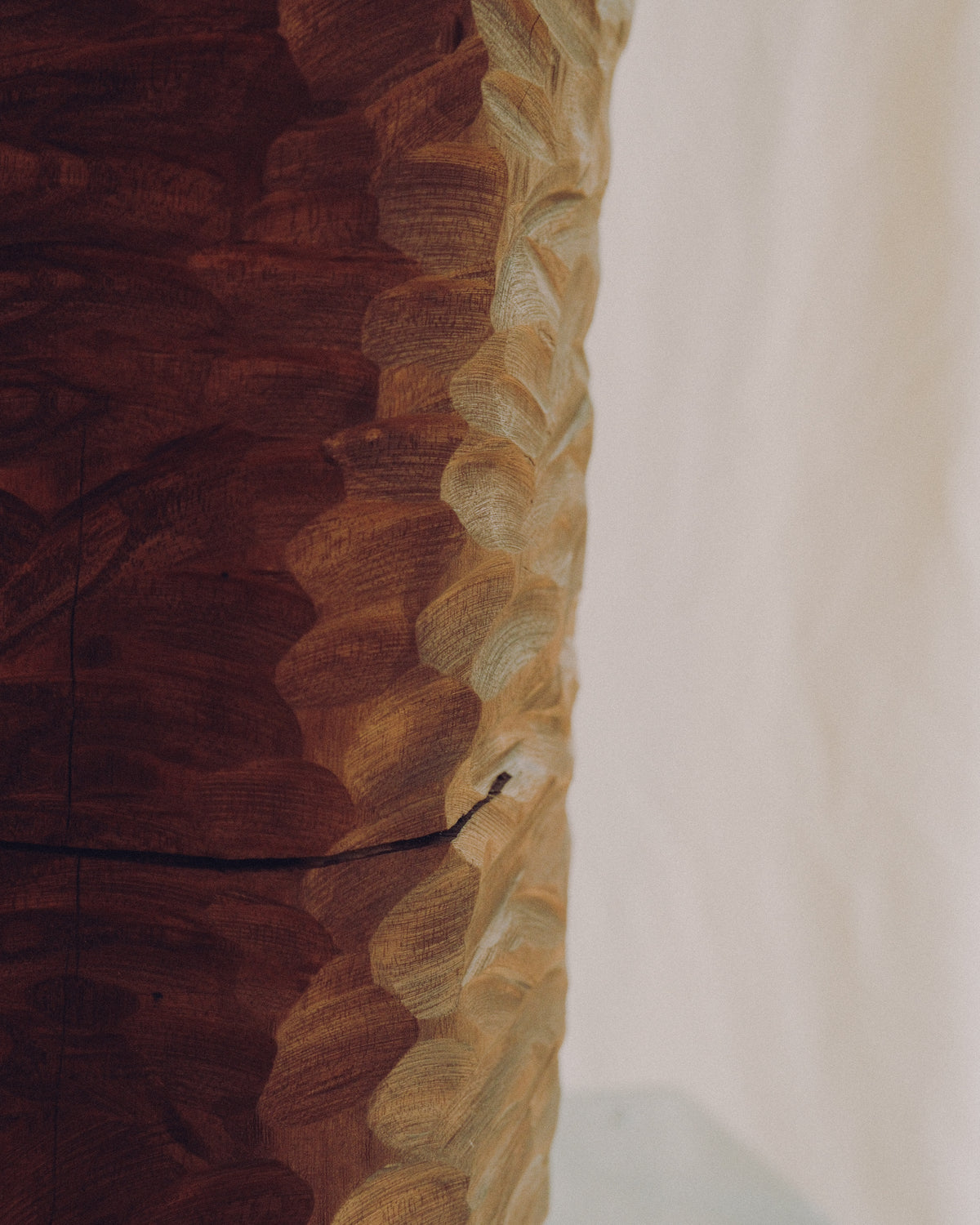 A close-up of a carved wooden object with a richly textured, wavy edge showing contrasting dark and light wood tones against a plain off-white background.