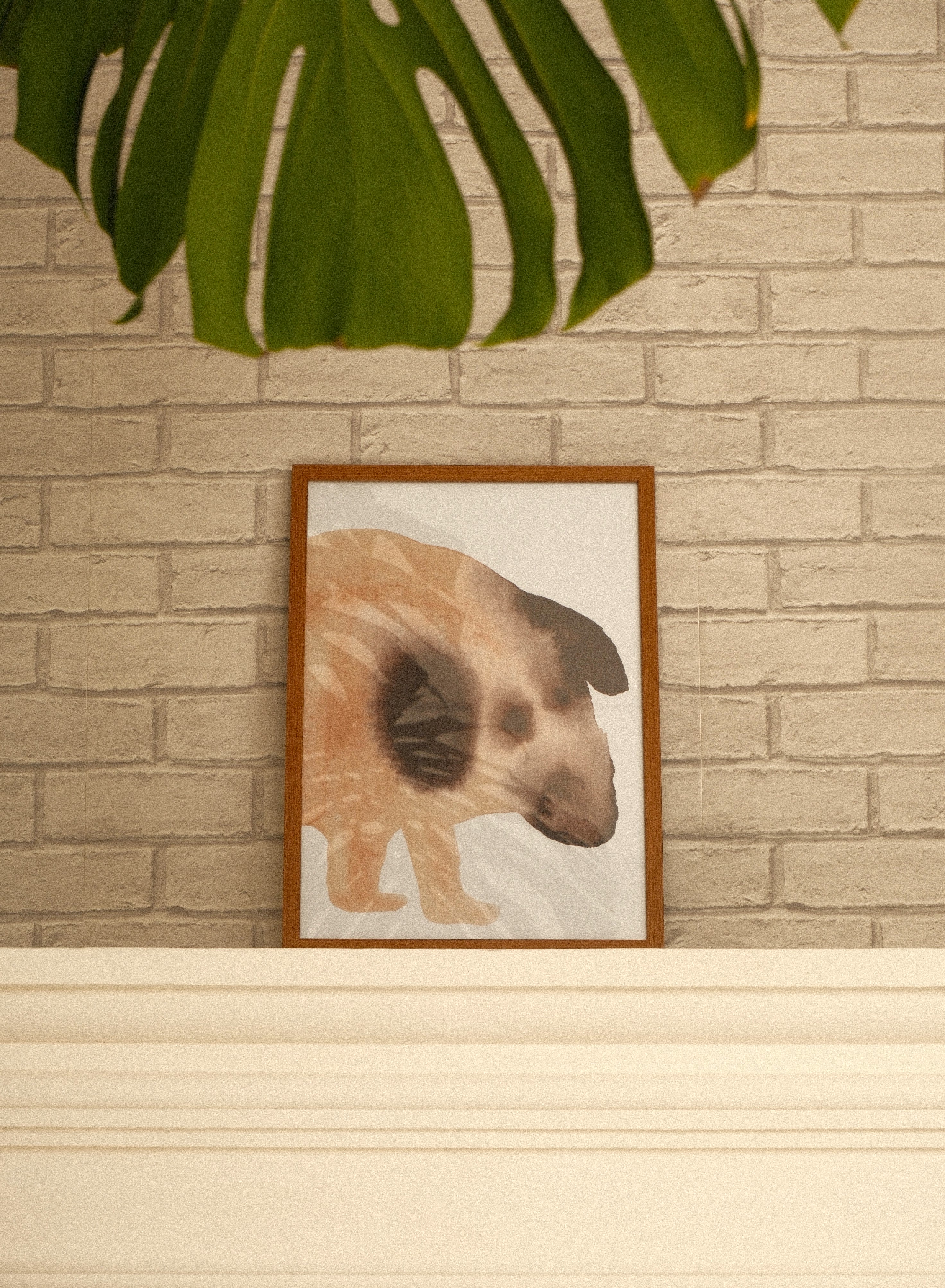 Framed artwork of a dog on a shelf against a brick wall.