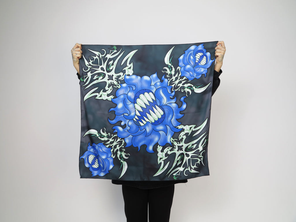 A person holding up a scarf with a floral pattern, predominantly blue flowers on a dark background.