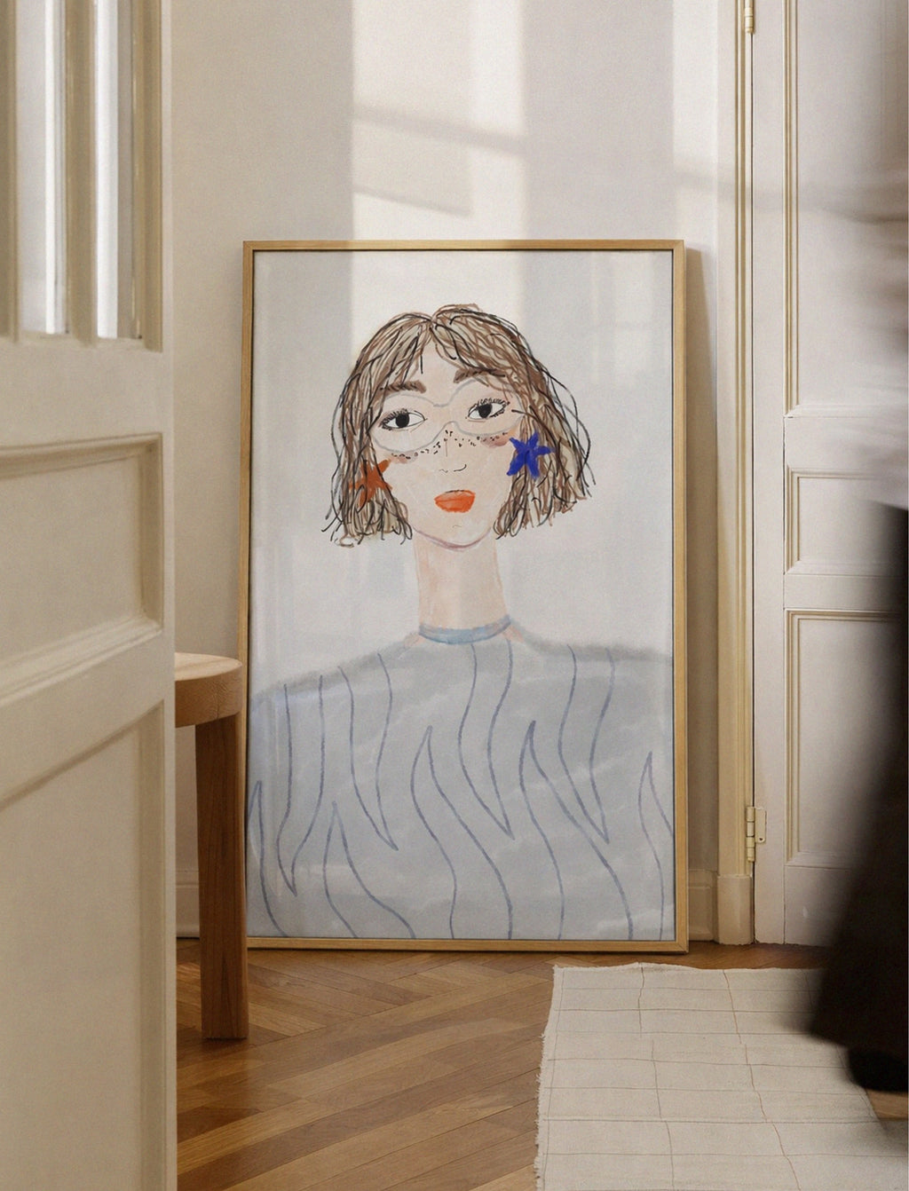Framed artwork of a stylized portrait on a wall in a room with wooden floor and white walls.