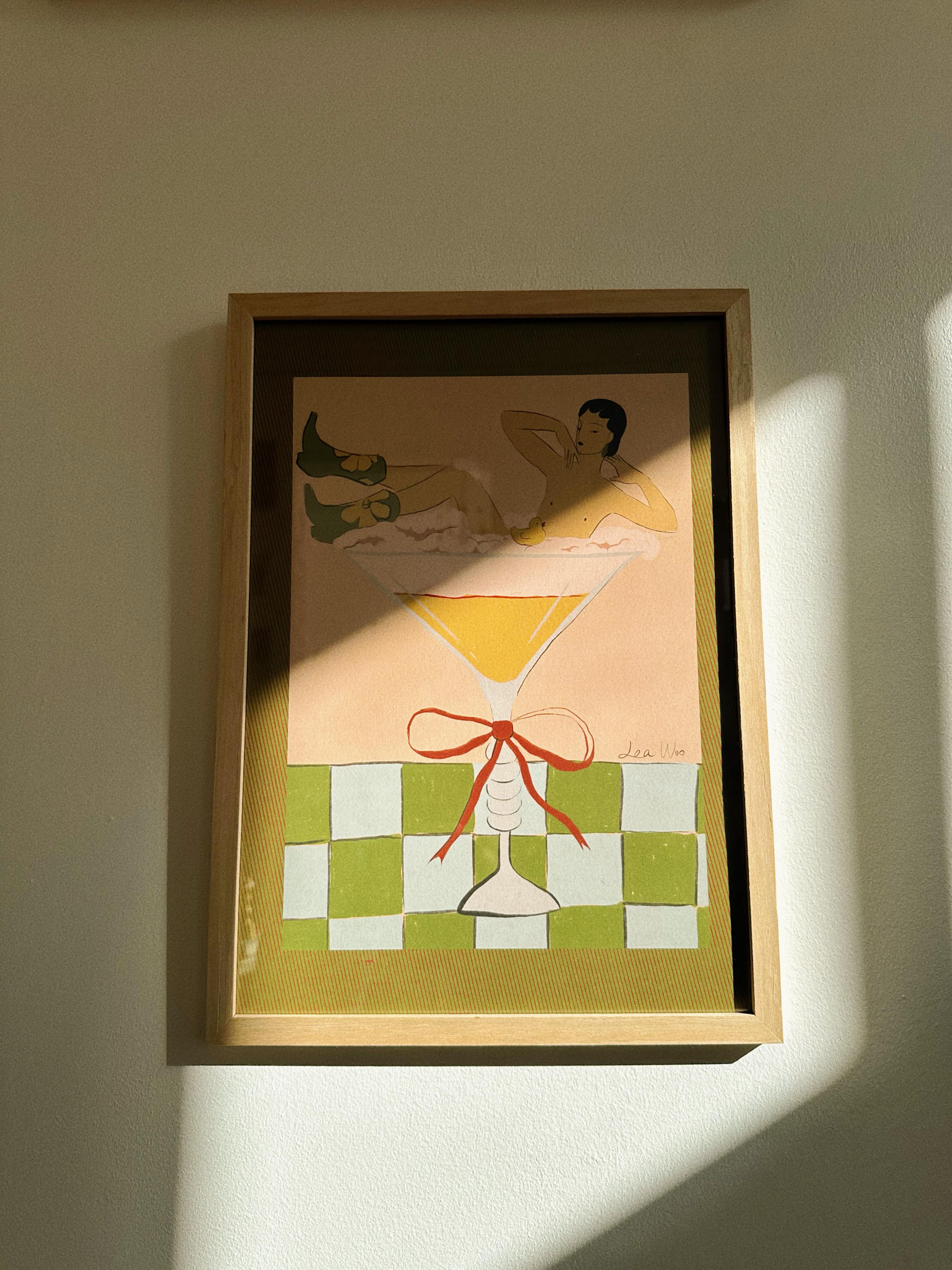 A framed poster featuring an illustration of a woman in a cocktail dress, with a design by Lea Woo. The artwork is characterized by soft colors and a nostalgic visual aesthetic.