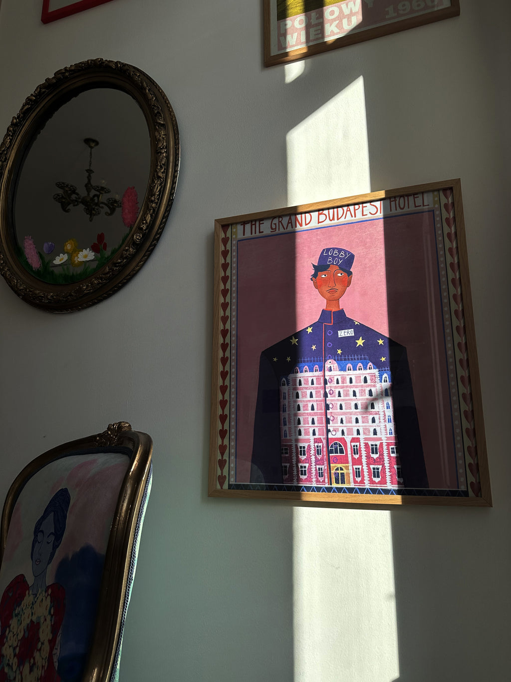 A framed poster of 'The Grand Budapest Hotel' featuring an illustration of a character in a uniform, displayed on a wall.  inspired by Wes Anderson’s film aesthetic