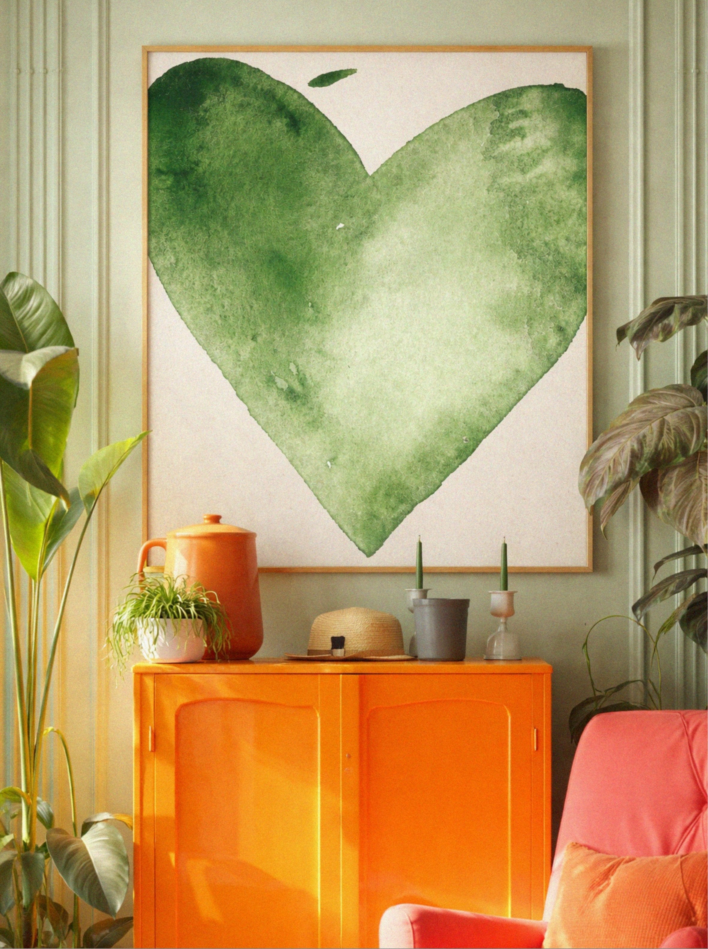 Heart-shaped green artwork on a wall with an orange cabinet and pink chair in a room.