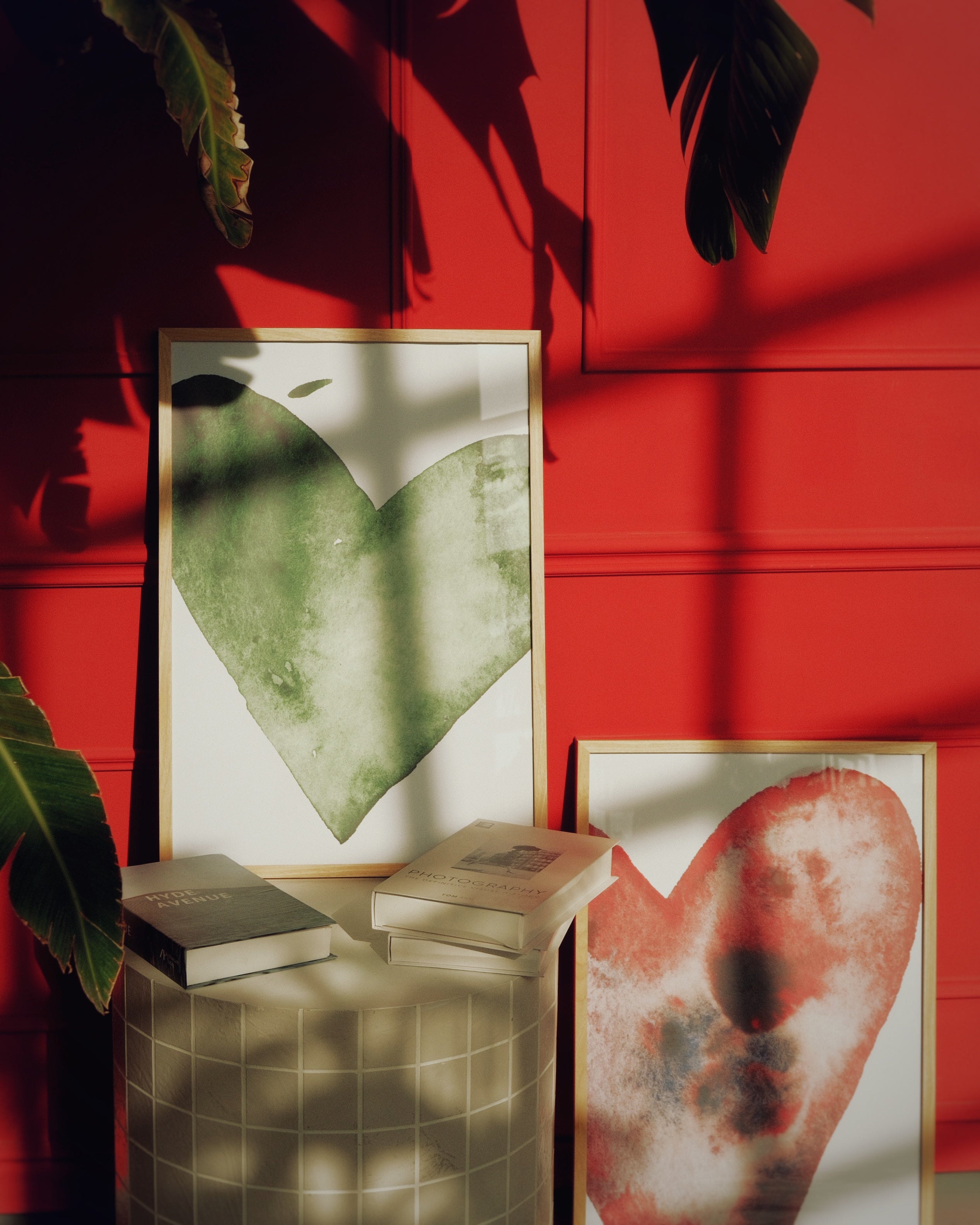 Framed artworks on a stand against a red wall with plant shadows