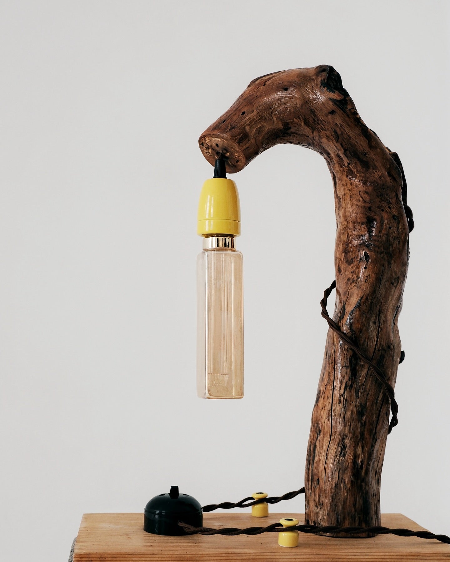 Lamp made from a wooden branch with a yellow bulb on a white background