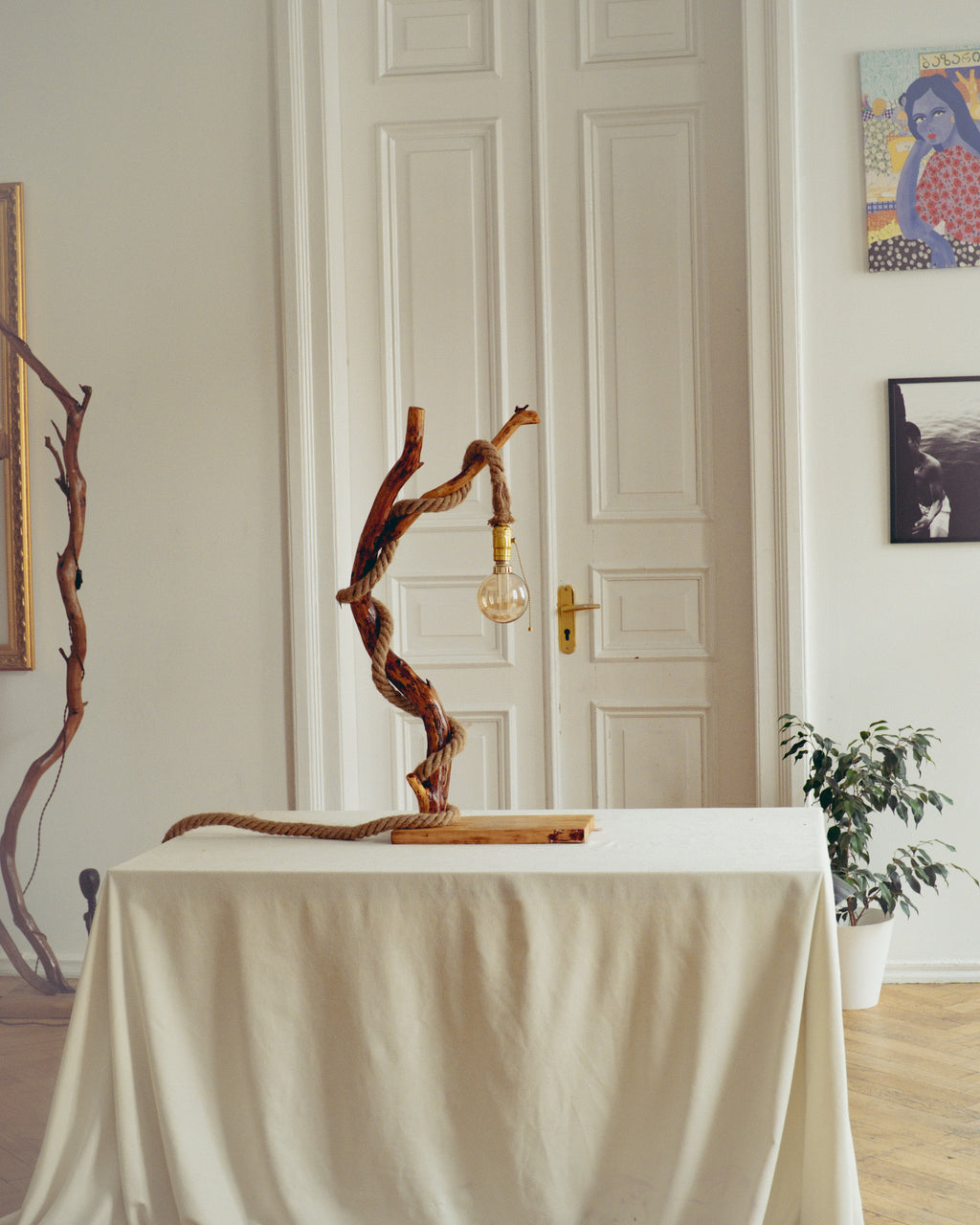 Decorative lamp with twisted branches on a table in a room with a white door and wall art.