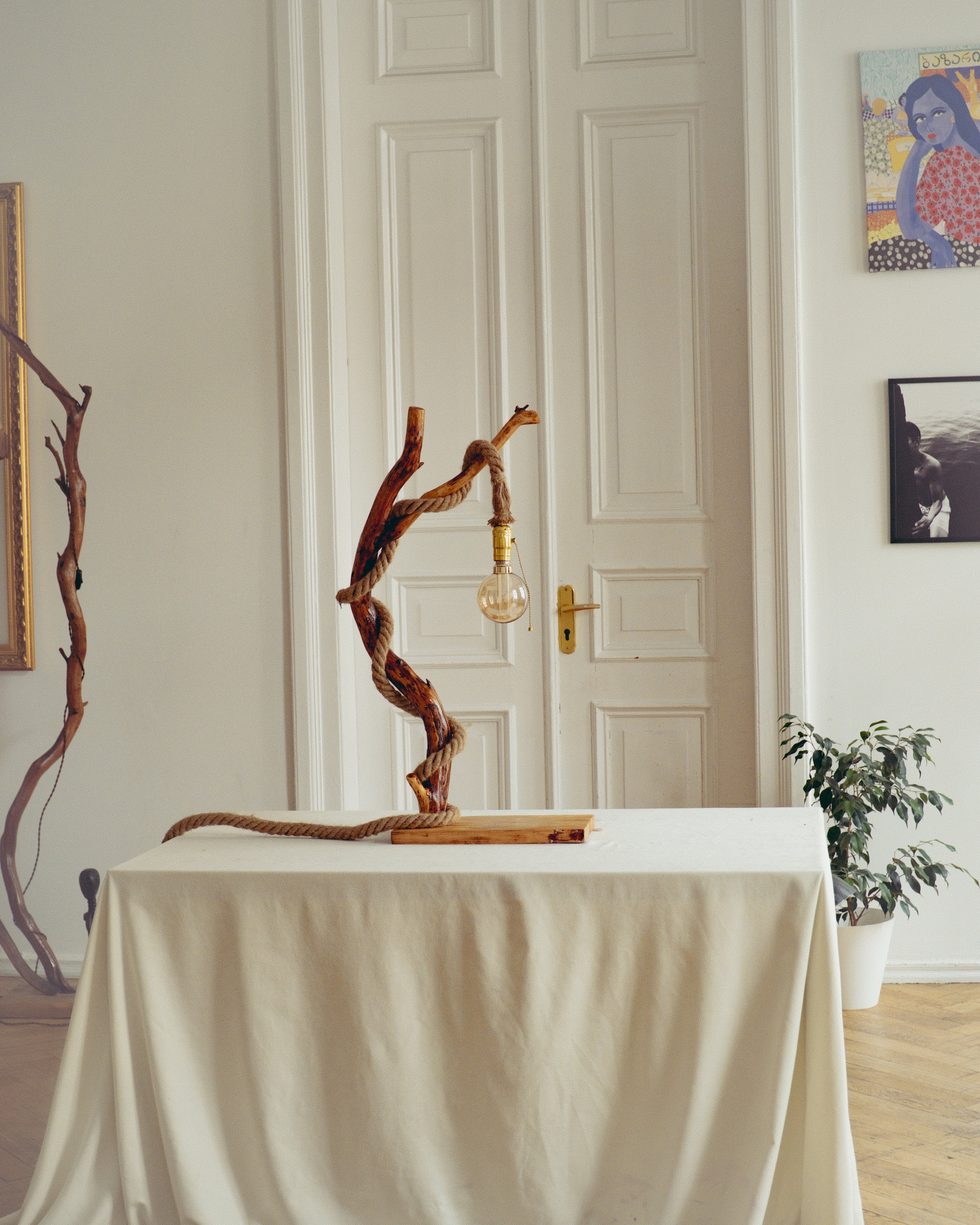 Decorative lamp with twisted branches on a table in a room with a white door and wall art.