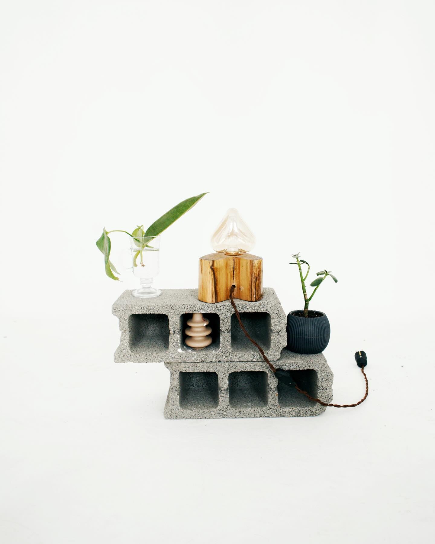 Concrete block shelf with decorative items on a white background, handmade wooden lamp from DAE on it