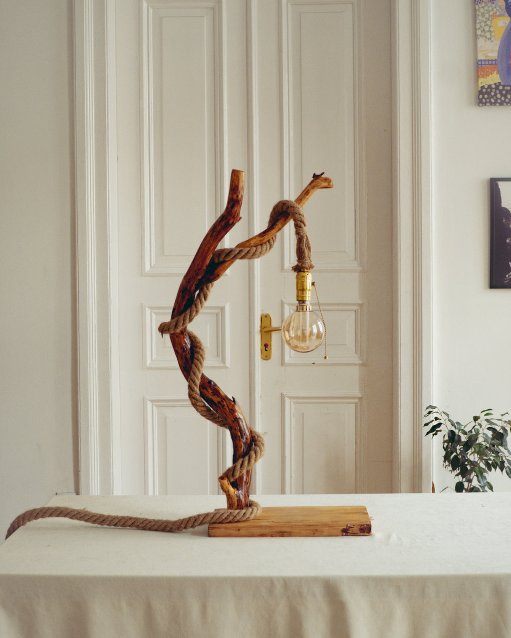 Driftwood lamp with a light bulb on a table against a neutral wall.