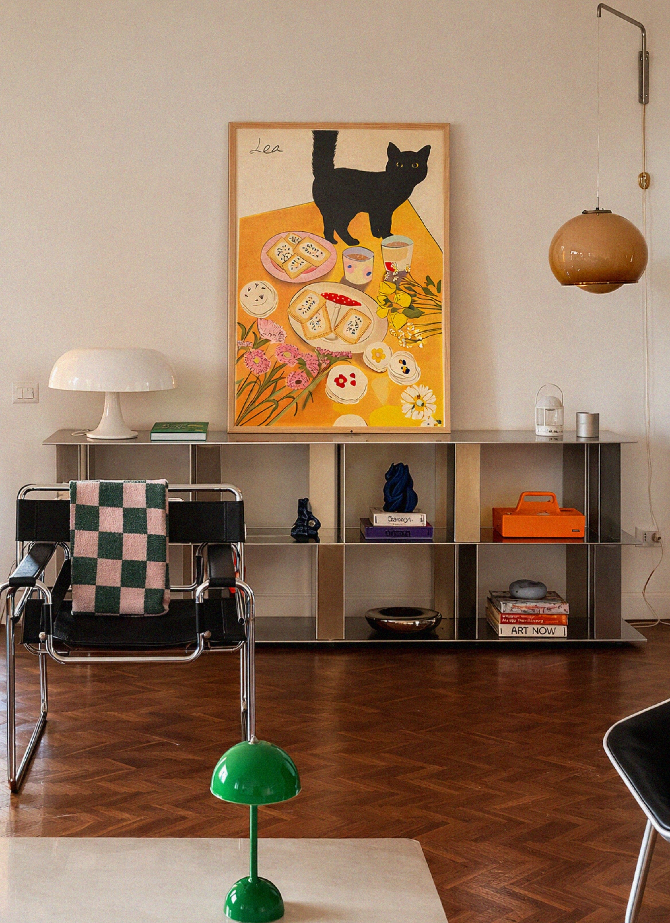 Modern interior with a black cat painting on the wall, a chair with a checkered blanket, and a green lamp.