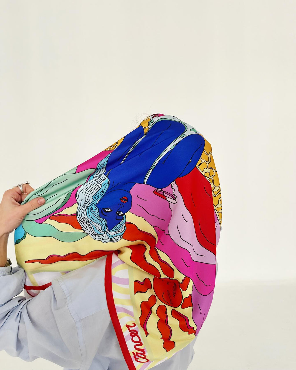 Colorful scarf with artistic design held by a person against a white background