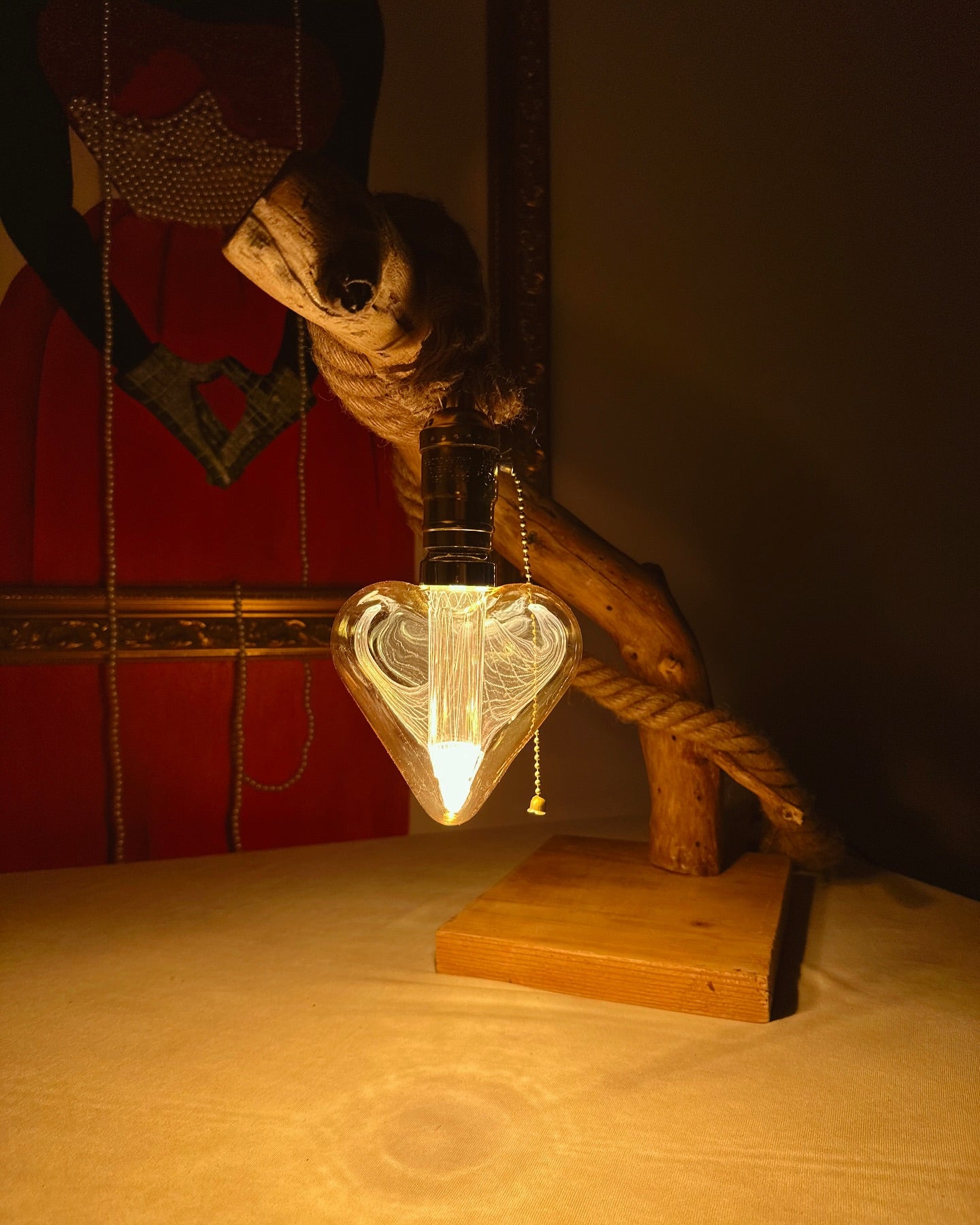 Handmade wooden table lamp with a heart-shaped bulb cover, placed on a flat surface with a textured background.