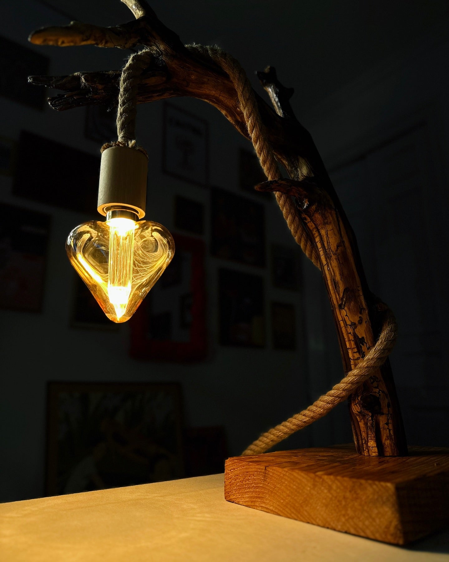 A handmade wooden lamp with a heart-shaped bulb and a rope hanging from the base, placed on a table.