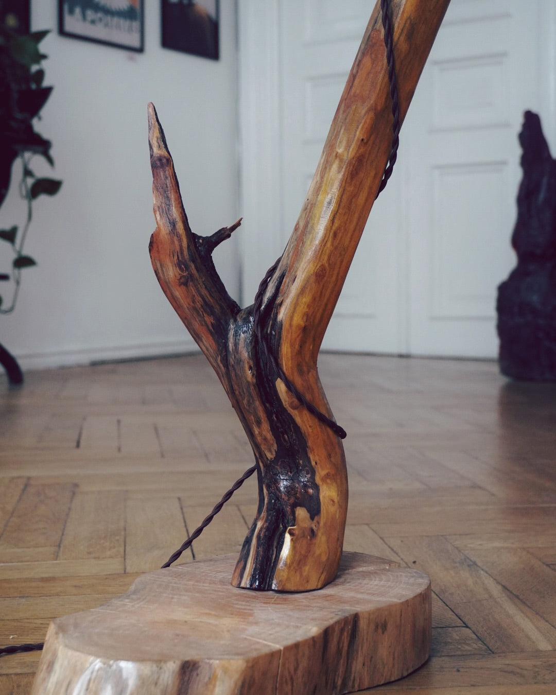 Wooden sculpture lamp on a wooden base in a room with a white wall and wooden floor.
