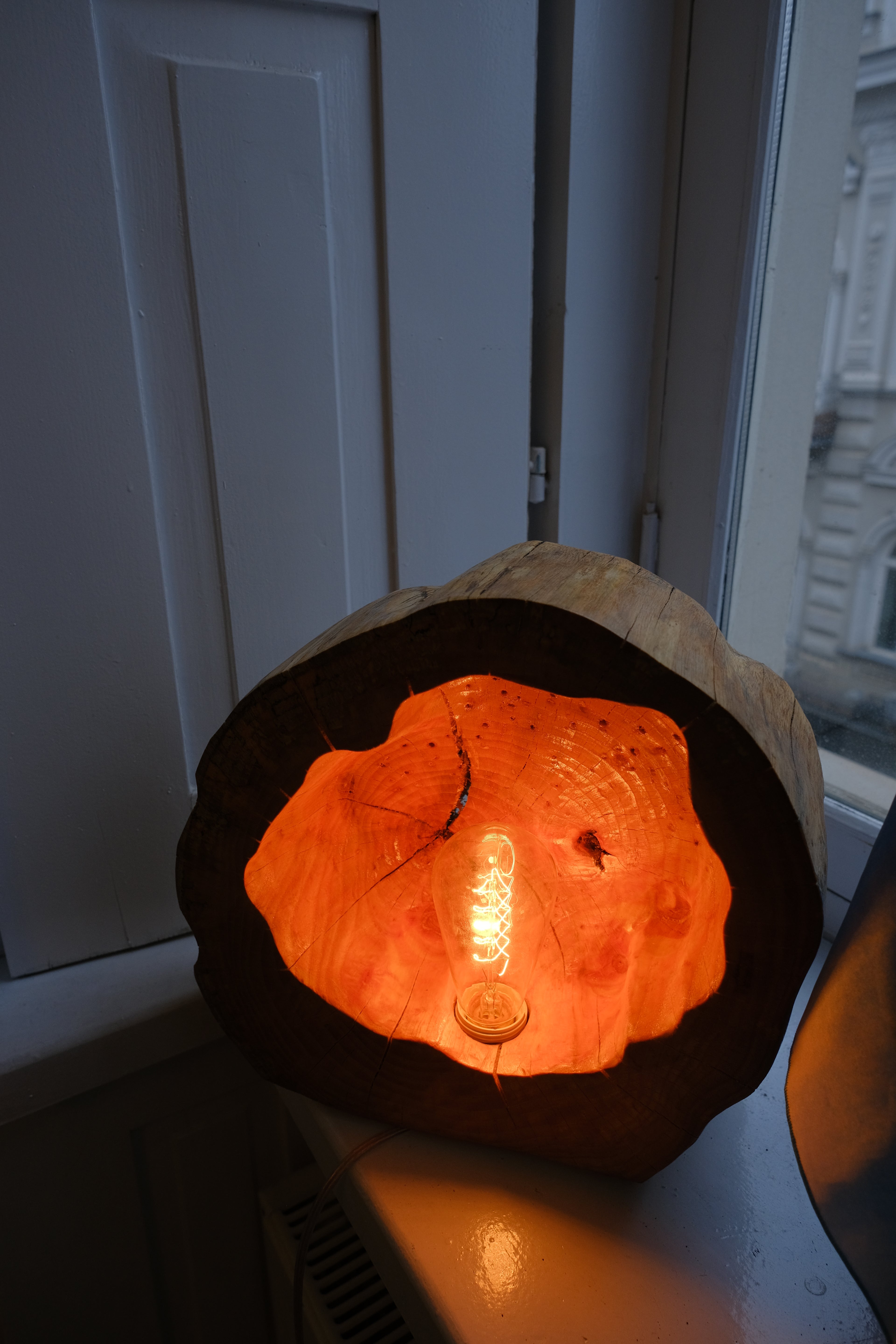 Handmade wooden lamp with a warm light glowing from within, placed near a window.